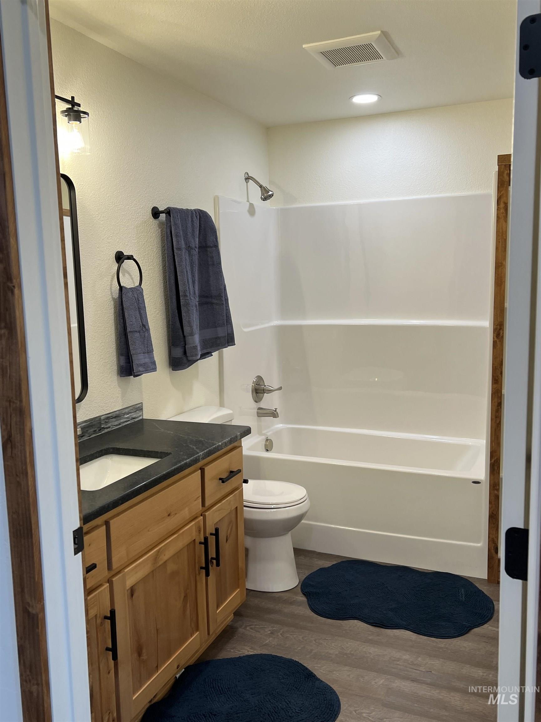 Full bath featuring dark wood-style flooring, shower / tub combination, vanity, and a textured wall