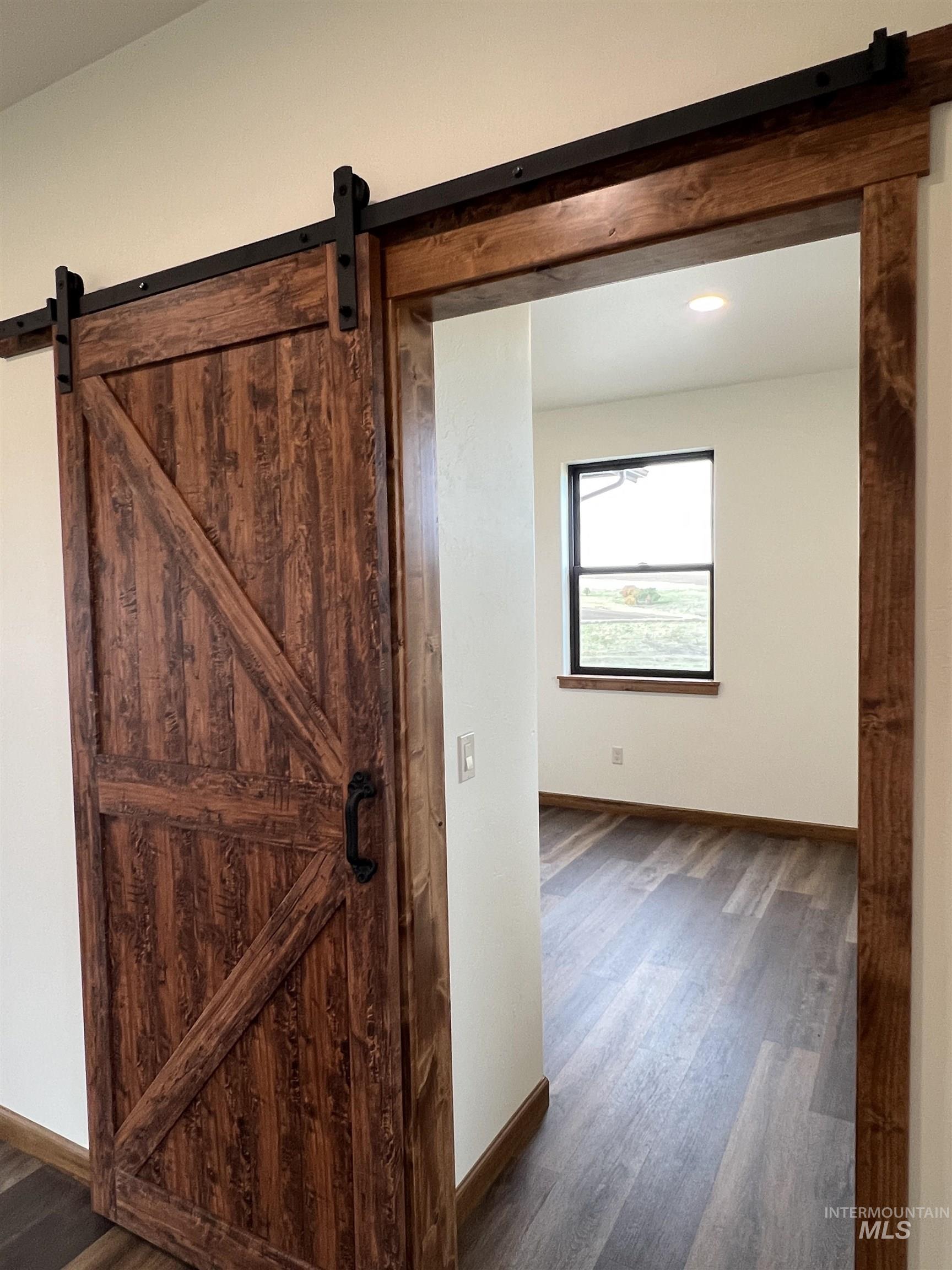 Corridor featuring a barn door and dark wood-style flooring