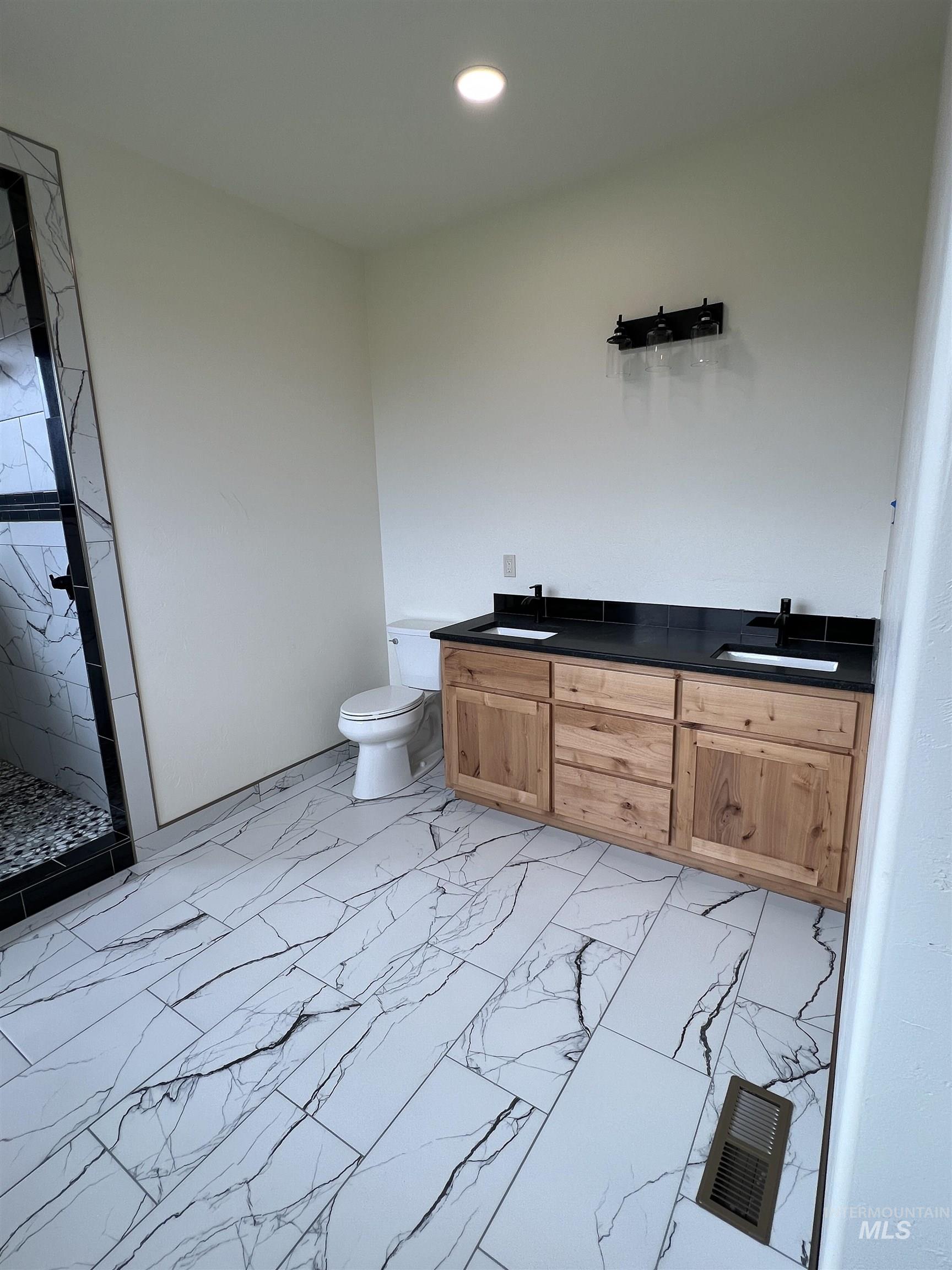 Bathroom featuring a marble finish shower, light marble finish floors, double vanity, and recessed lighting