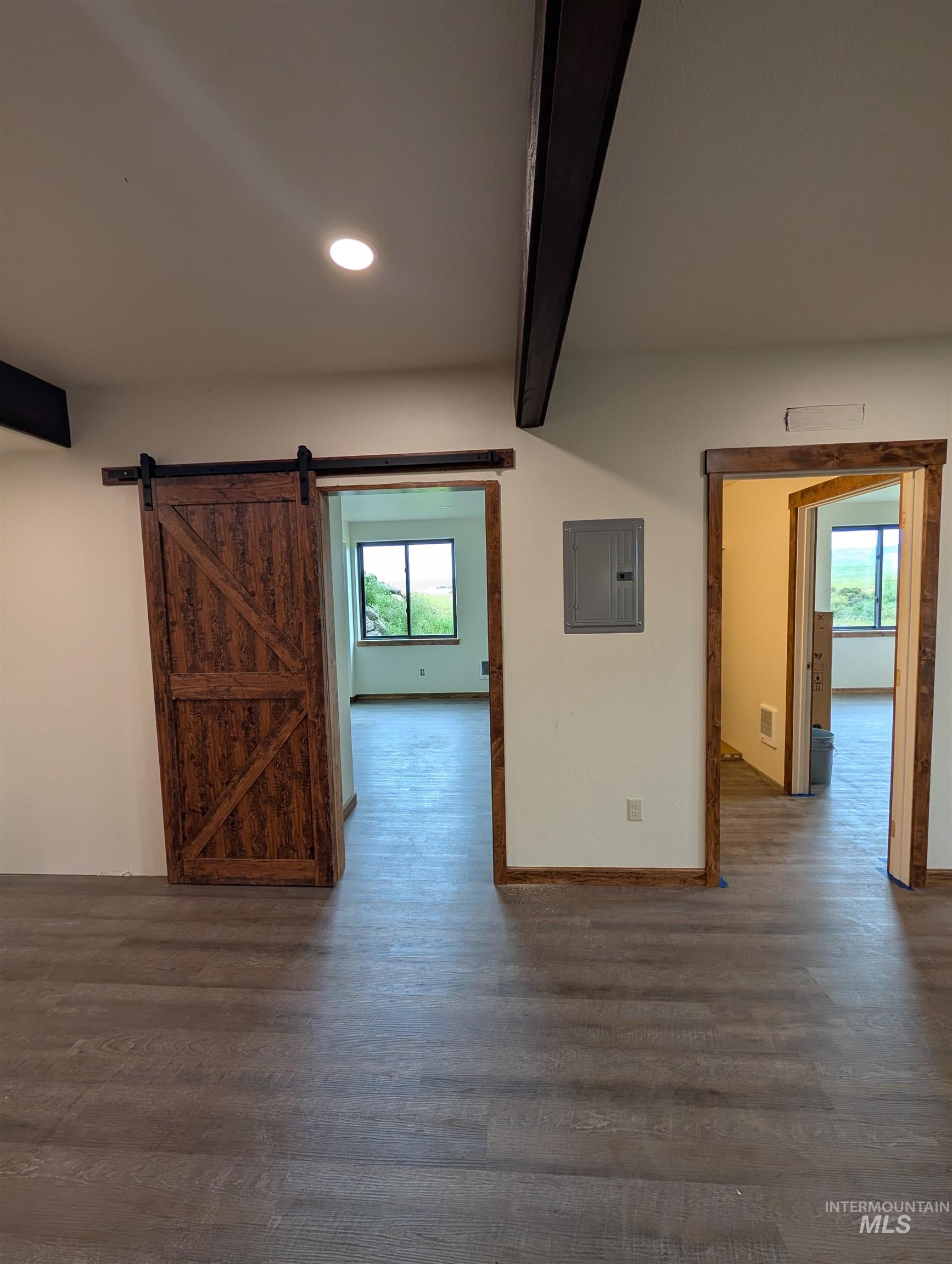 Empty room featuring beamed ceiling, wood finished floors, a barn door, electric panel, and recessed lighting