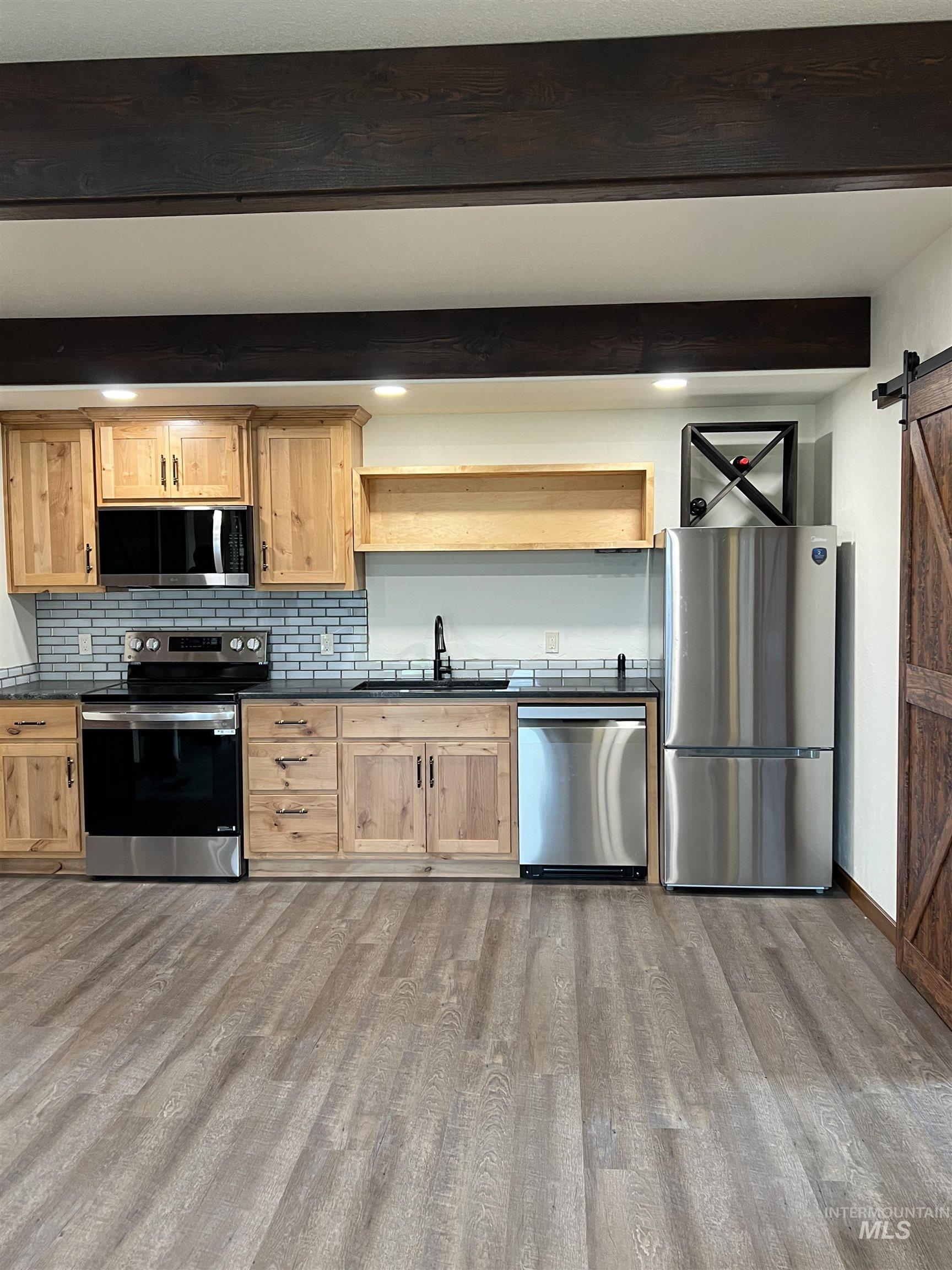Kitchen with a barn door, open shelves, beam ceiling, stainless steel appliances, and dark countertops