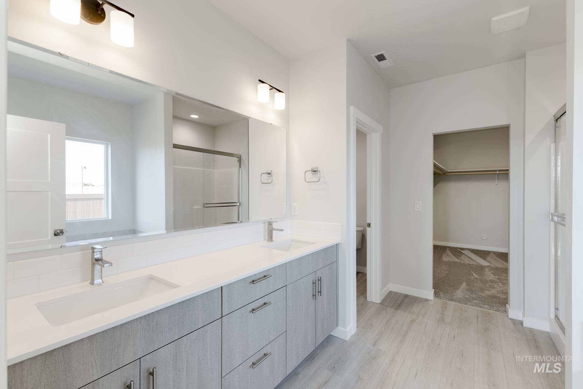 Bathroom with a stall shower, a spacious closet, double vanity, and light wood finished floors