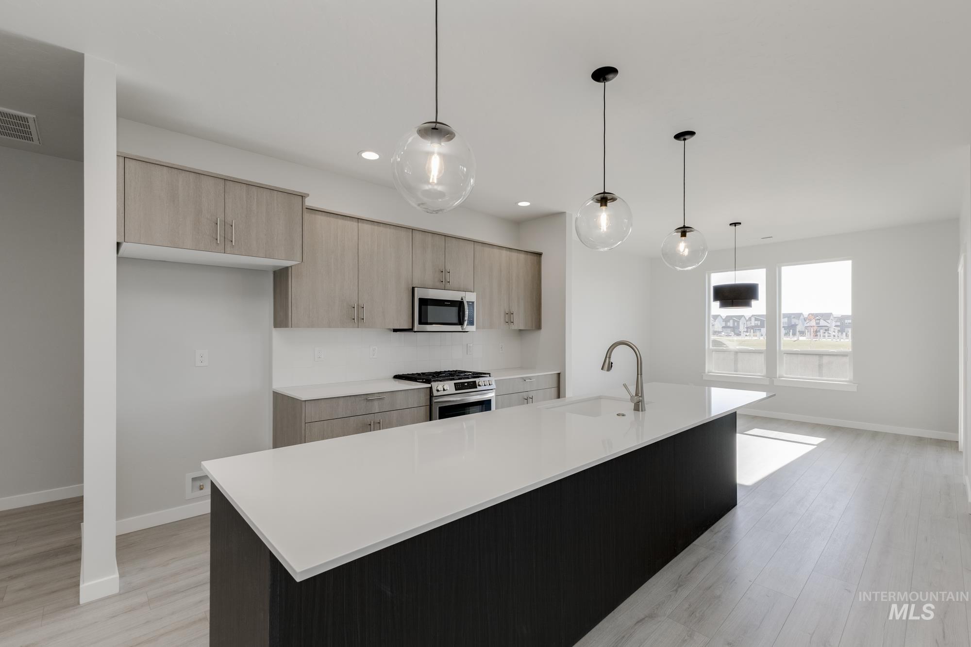 Kitchen featuring a center island with sink, pendant lighting, modern cabinets, appliances with stainless steel finishes, and light stone countertops