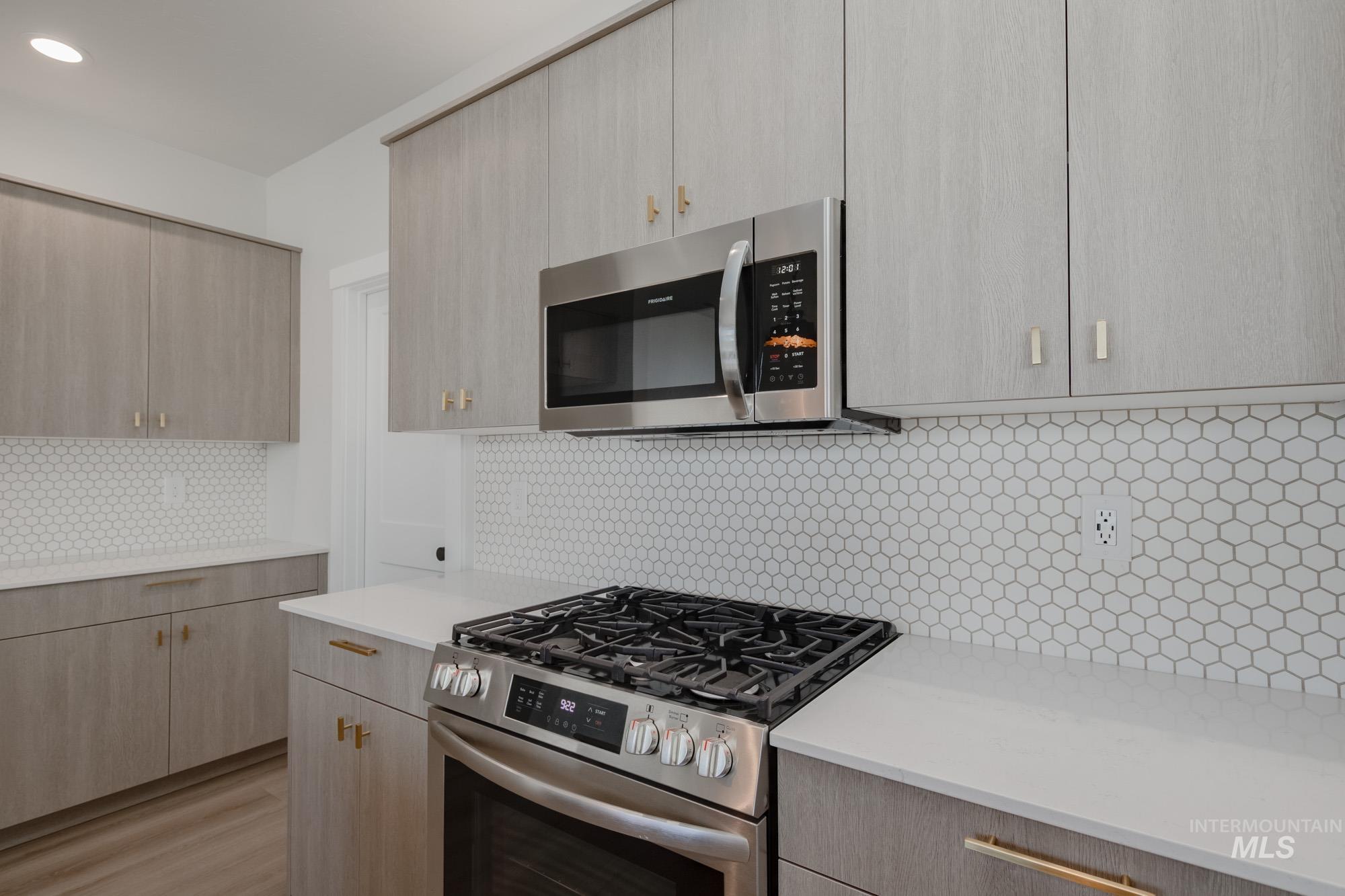 Kitchen with appliances with stainless steel finishes, light brown cabinetry, tasteful backsplash, modern cabinets, and light stone counters