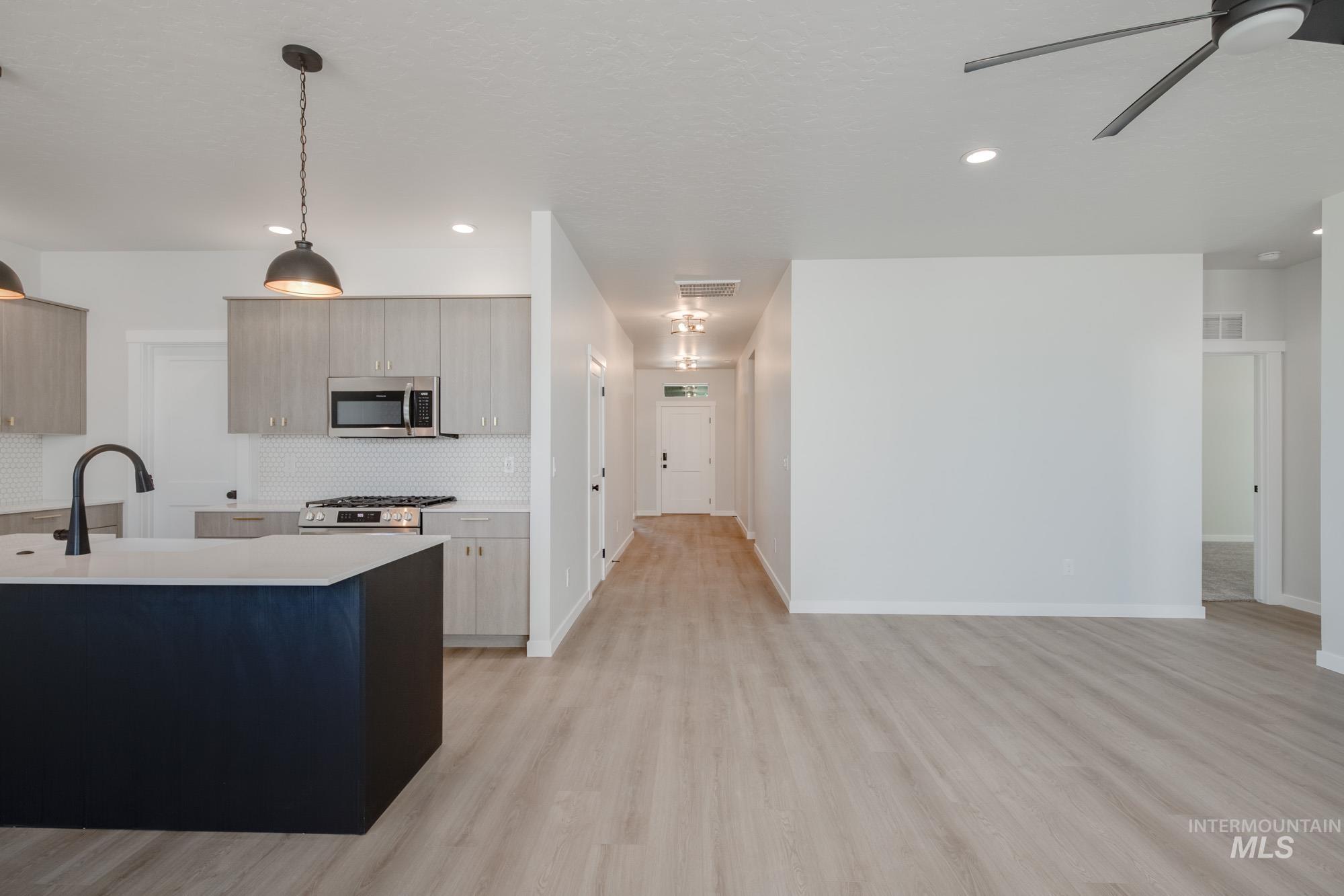 Kitchen featuring decorative backsplash, light wood-style flooring, hanging light fixtures, ceiling fan, and appliances with stainless steel finishes