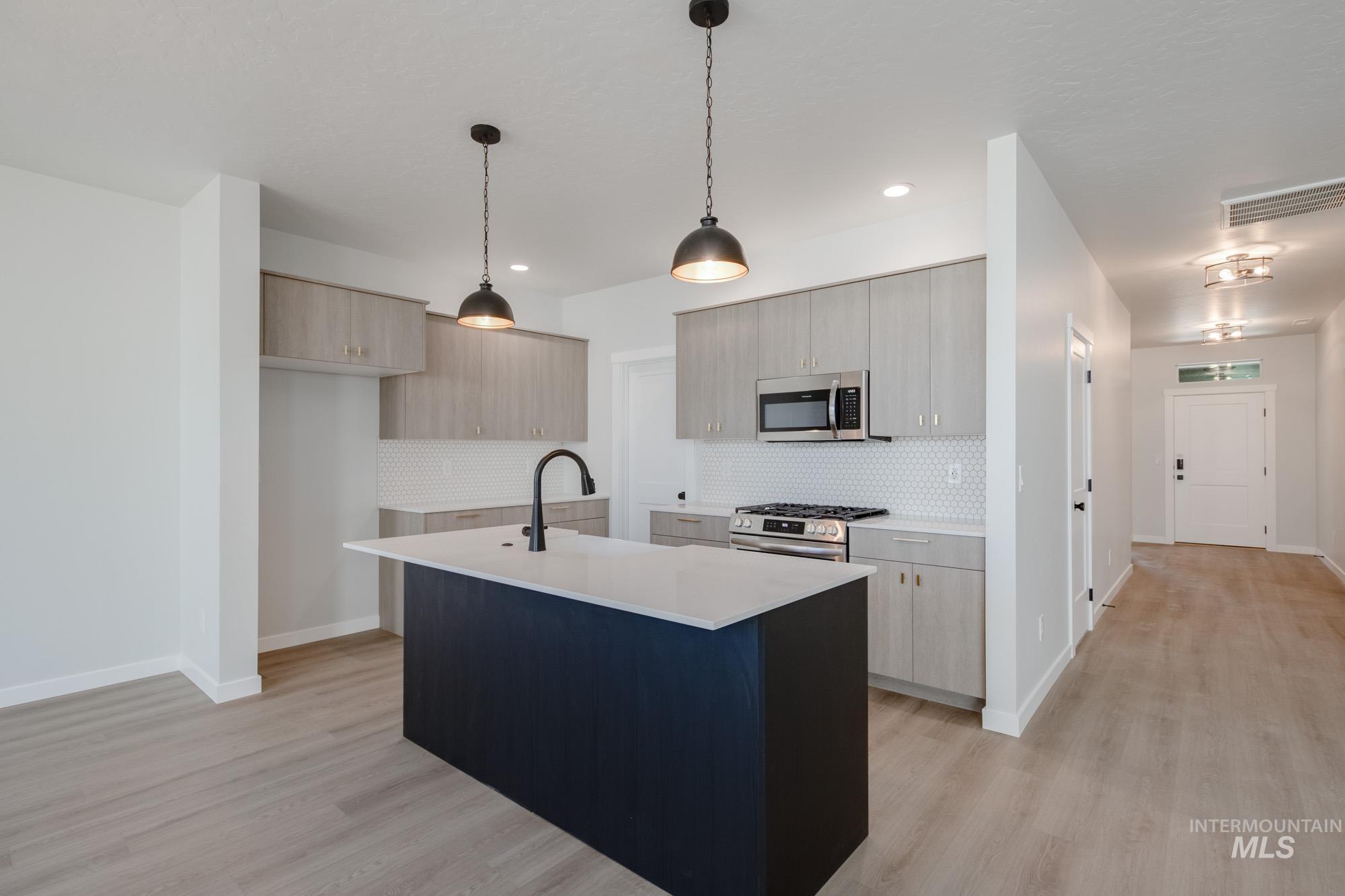 Kitchen with modern cabinets, decorative light fixtures, a center island with sink, light wood-style floors, and recessed lighting