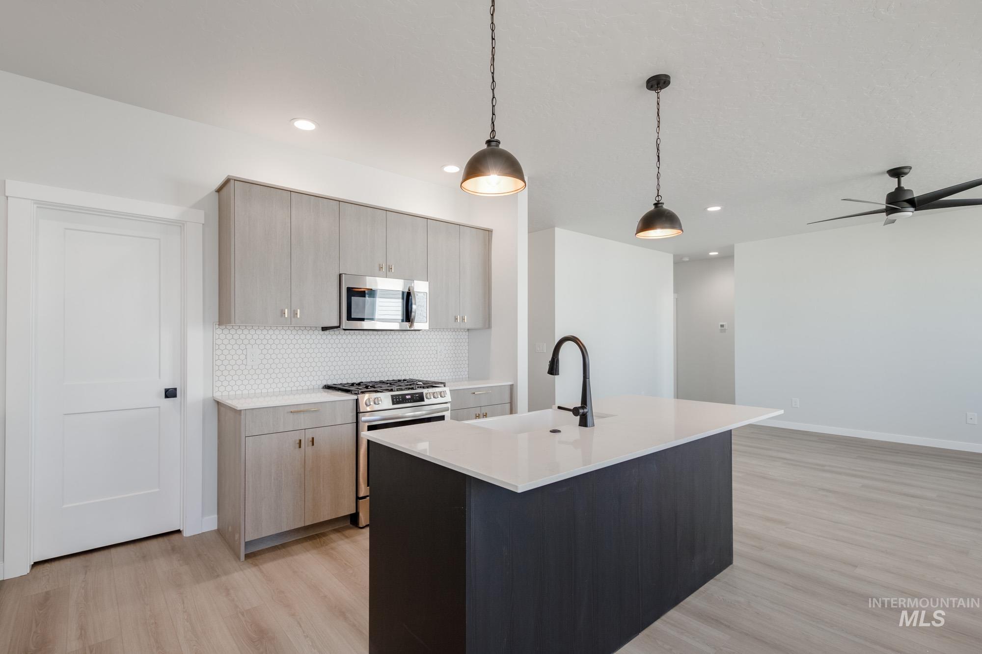 Kitchen with appliances with stainless steel finishes, an island with sink, light wood finished floors, decorative light fixtures, and decorative backsplash
