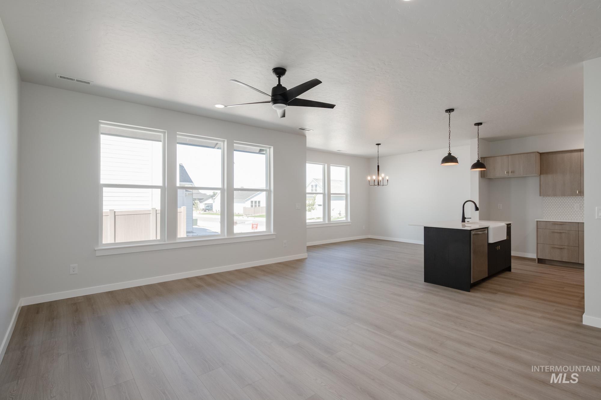 Unfurnished living room featuring light wood-style floors, a ceiling fan, and a chandelier
