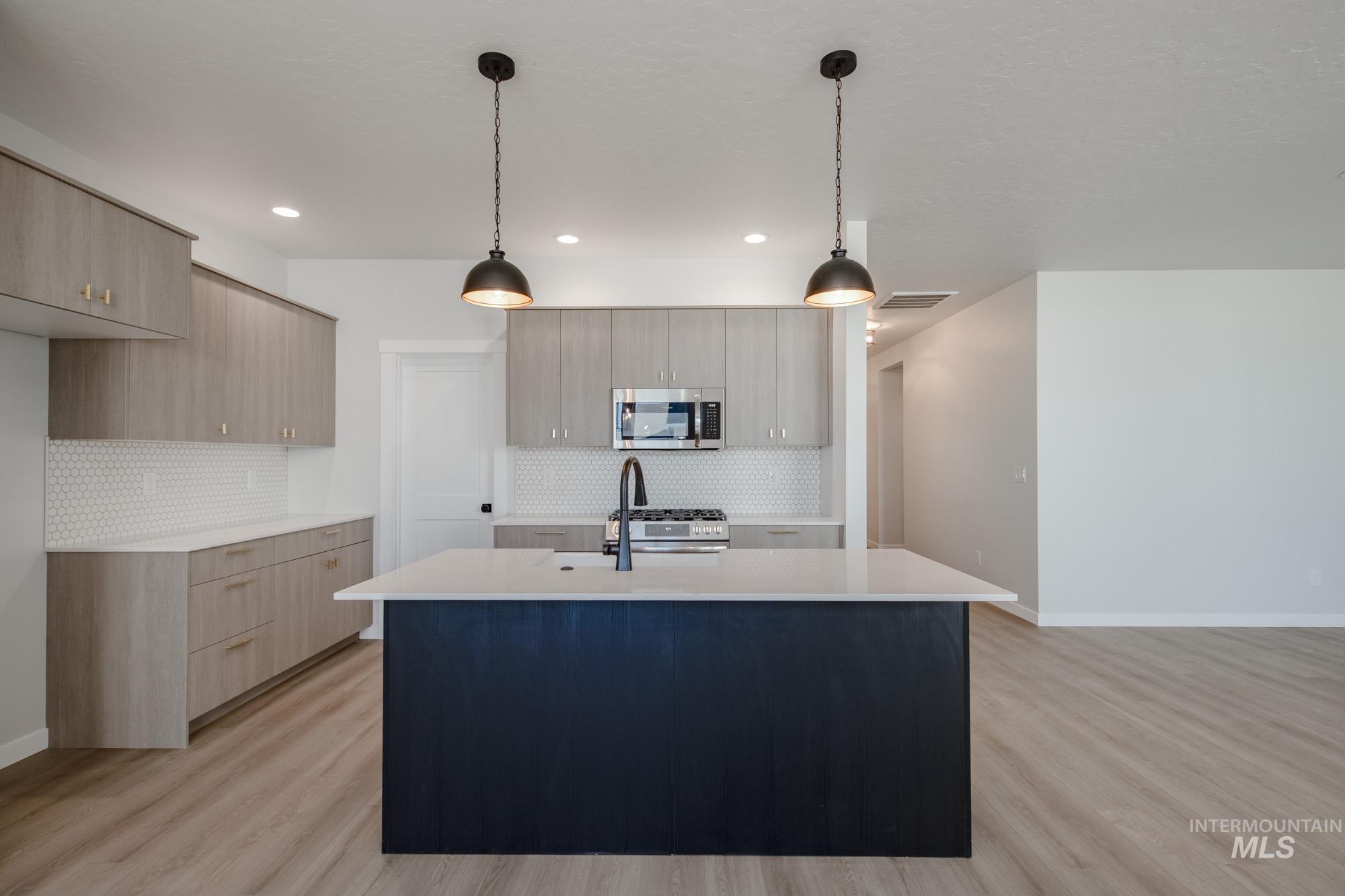 Kitchen with modern cabinets, pendant lighting, light wood-style floors, a kitchen island with sink, and recessed lighting