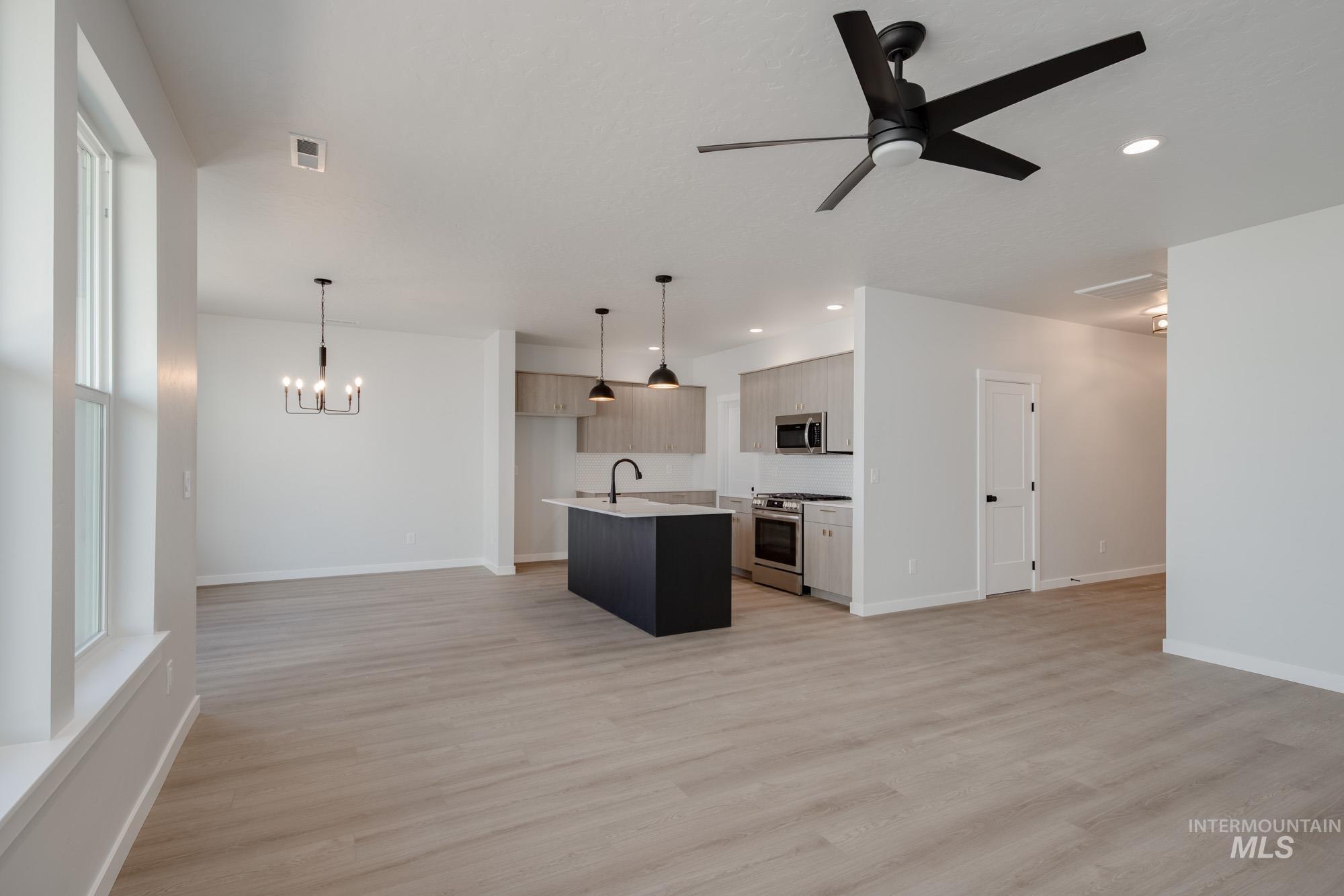 Kitchen with open floor plan, decorative light fixtures, an island with sink, light wood-style floors, and recessed lighting