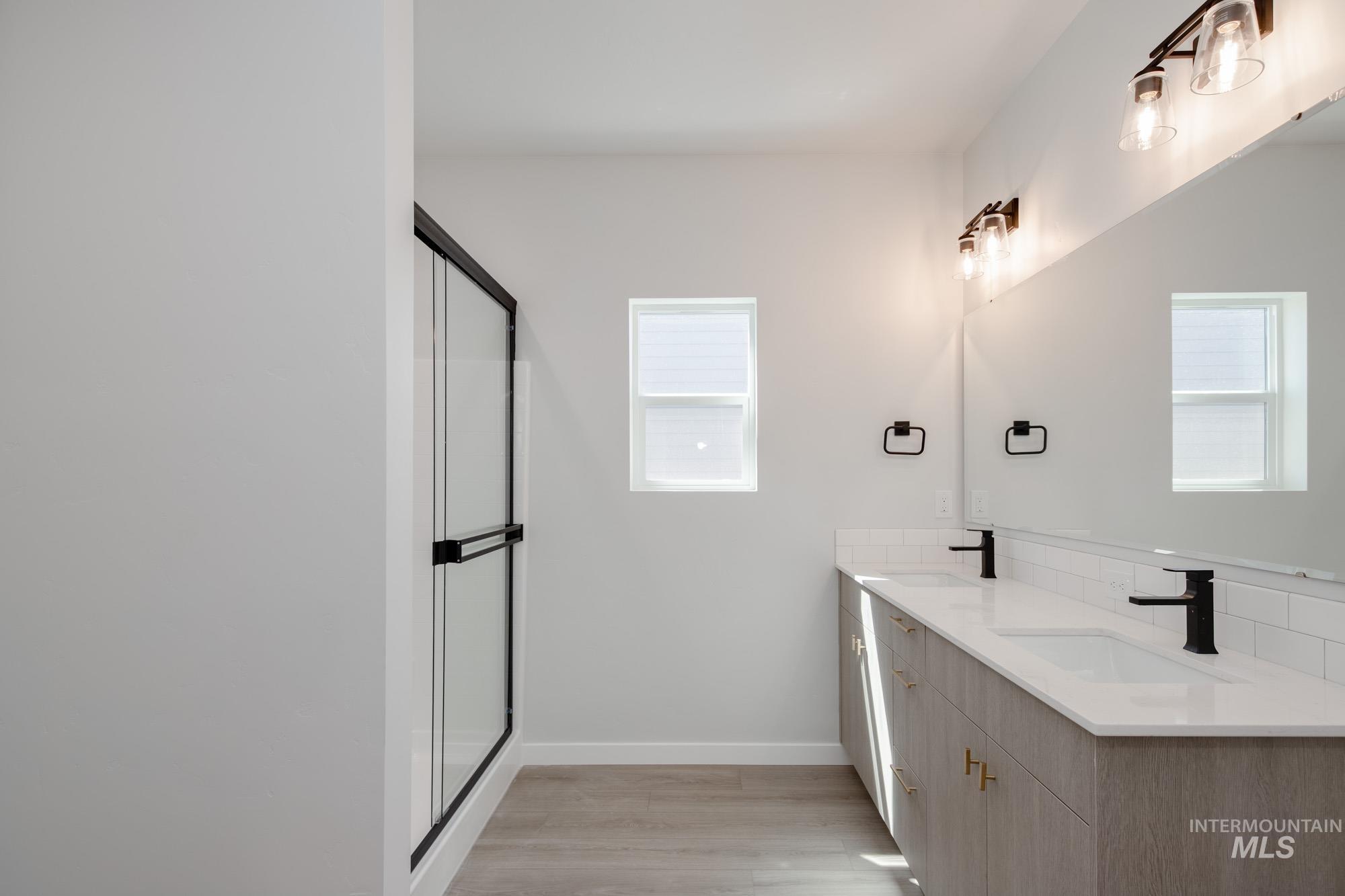 Bathroom with double vanity, a stall shower, and light wood-type flooring