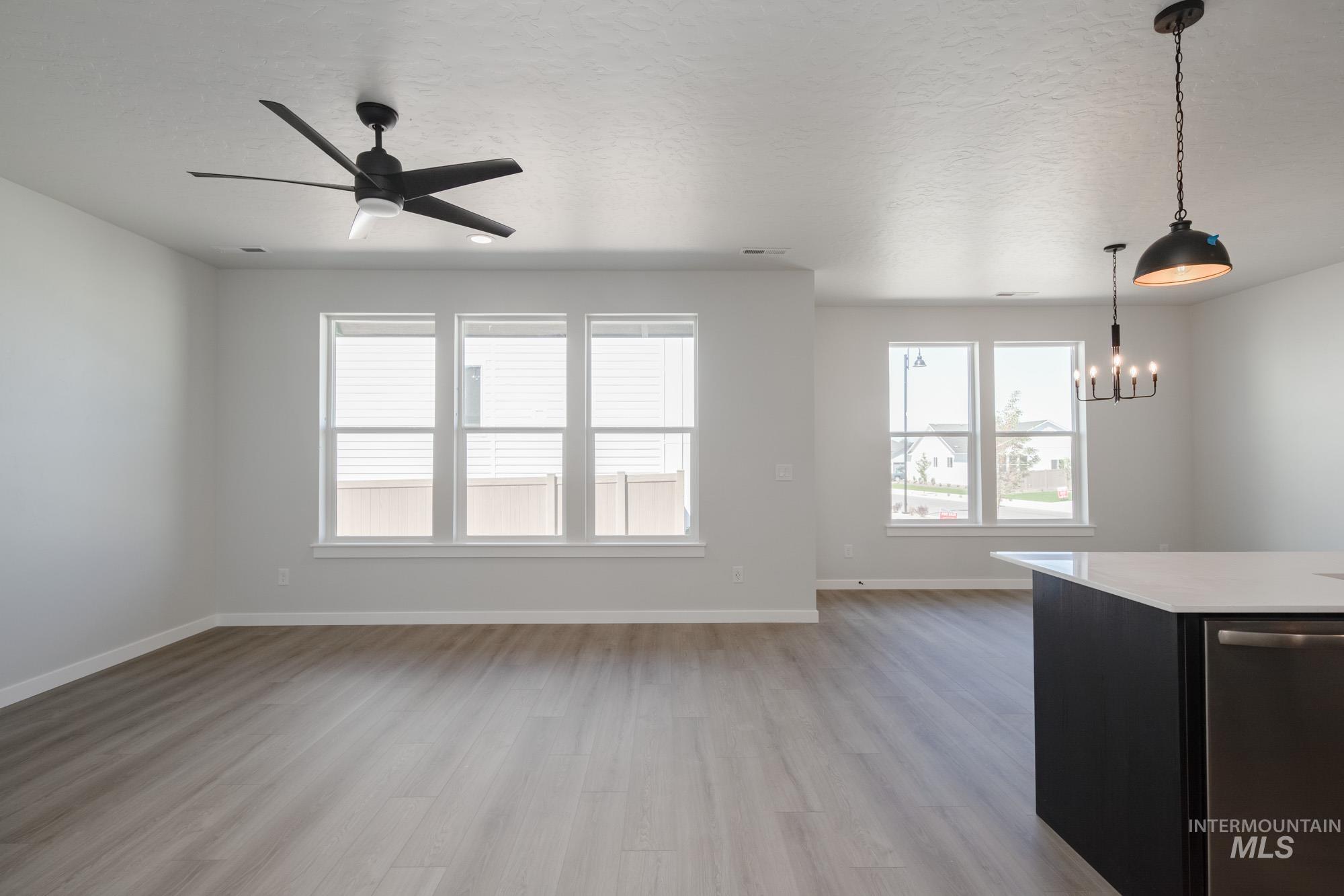 Unfurnished living room featuring light wood-style floors, a textured ceiling, a ceiling fan, and a chandelier