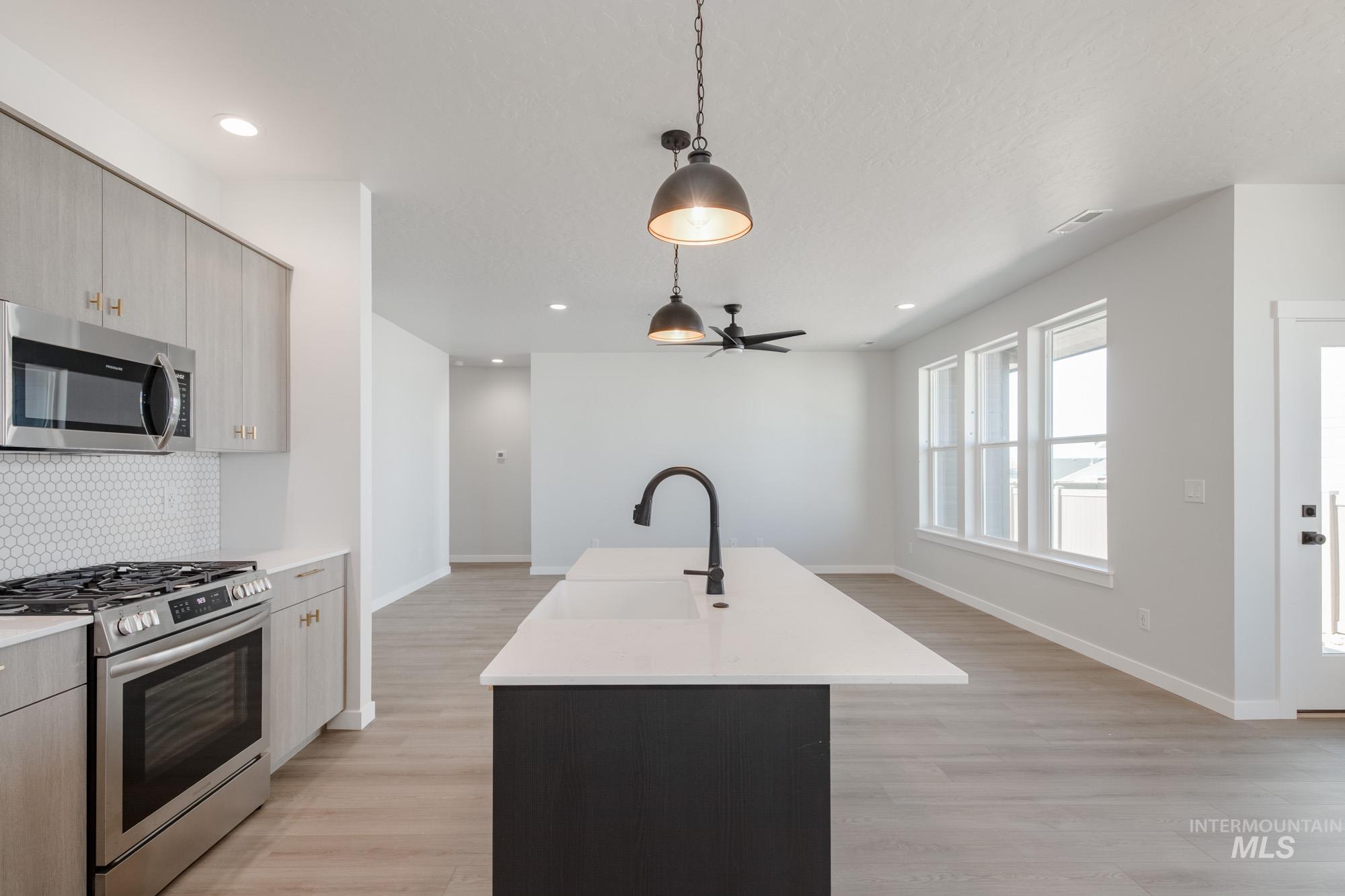 Kitchen with stainless steel appliances, pendant lighting, decorative backsplash, light wood finished floors, and a center island with sink