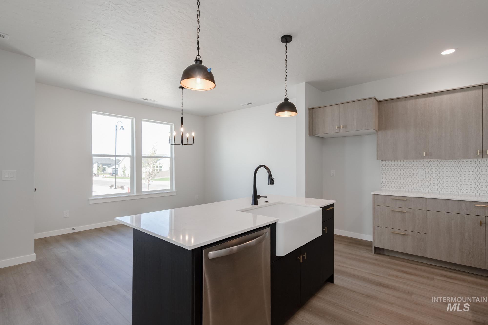 Kitchen featuring dishwasher, light wood-type flooring, decorative light fixtures, and dark cabinetry