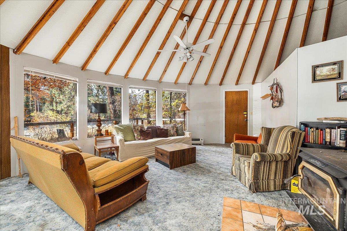 Sunroom featuring high vaulted ceiling, beam ceiling, carpet flooring, and a wood stove
