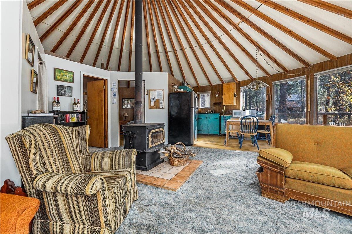 Living area with a wood stove, carpet flooring, high vaulted ceiling, beam ceiling, and wooden walls