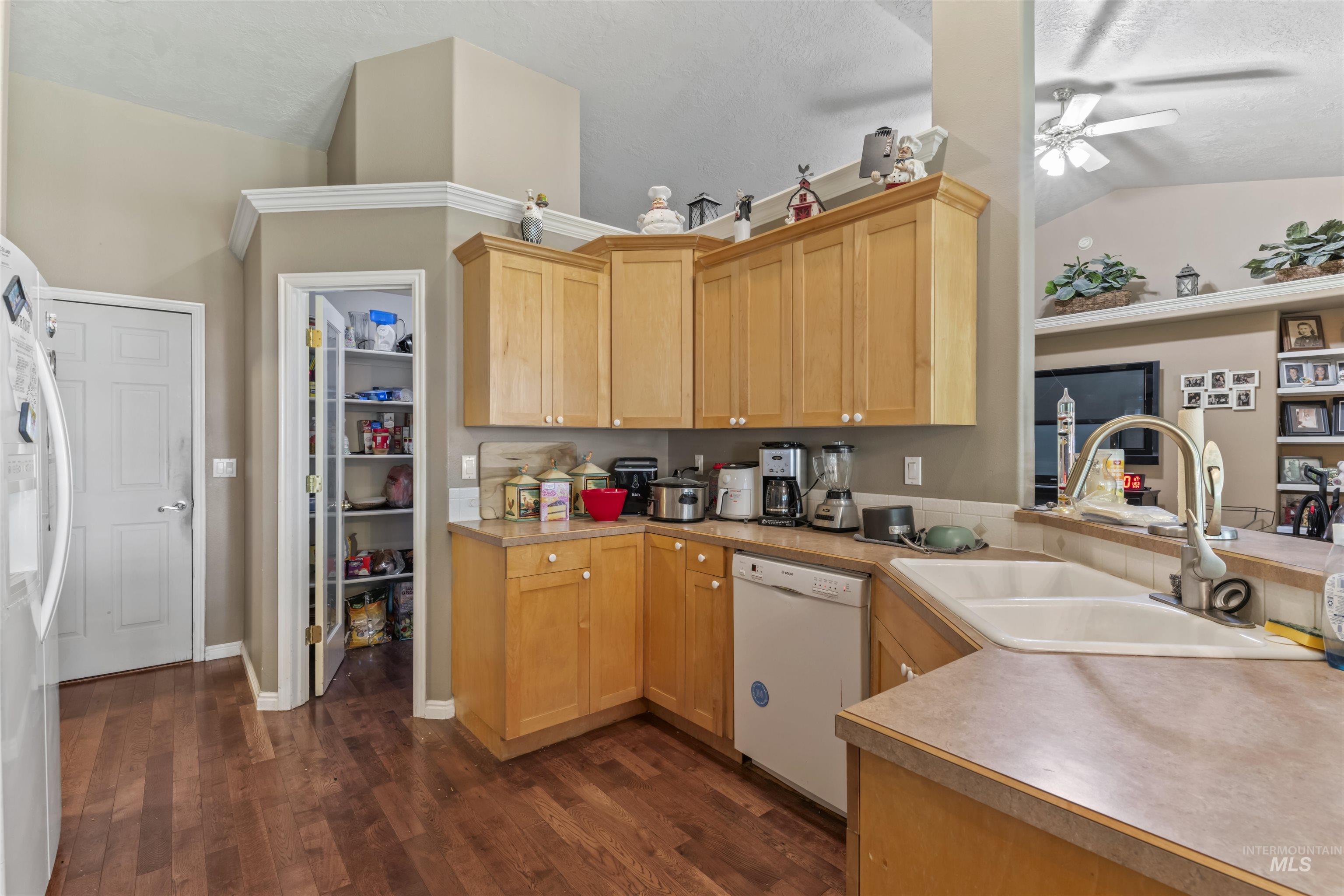 Kitchen with light countertops, white dishwasher, dark wood-style floors, freestanding refrigerator, and vaulted ceiling