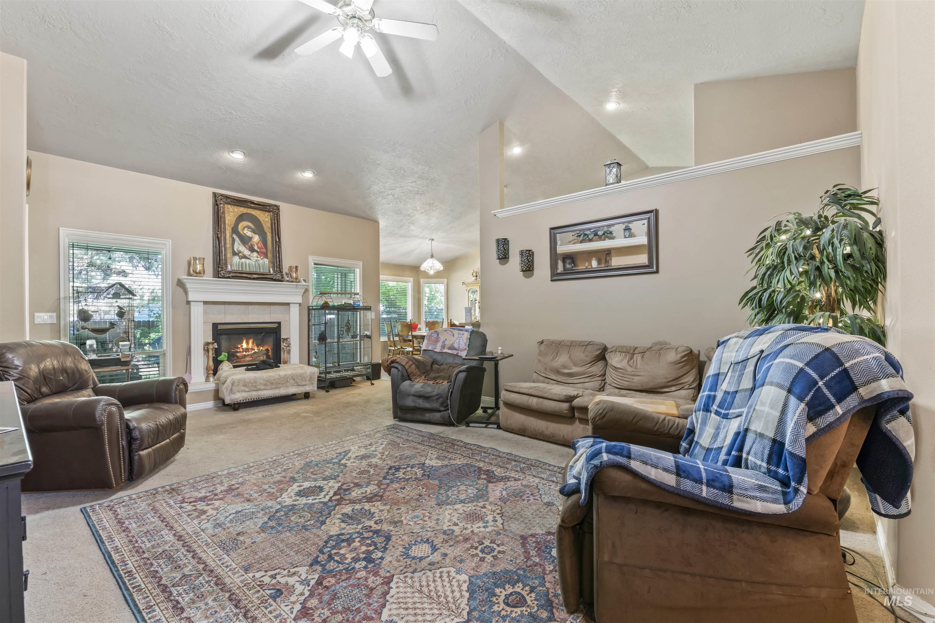 Carpeted living room featuring high vaulted ceiling, ceiling fan, a fireplace, a textured ceiling, and recessed lighting