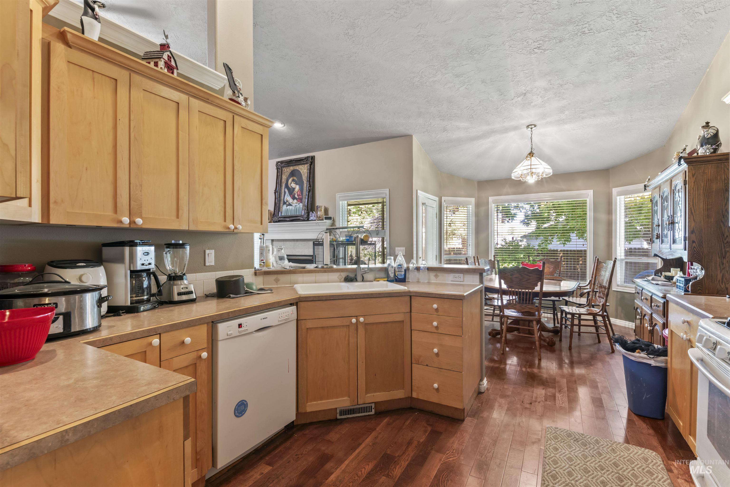 Kitchen featuring dark wood-type flooring, white appliances, light countertops, a peninsula, and a textured ceiling