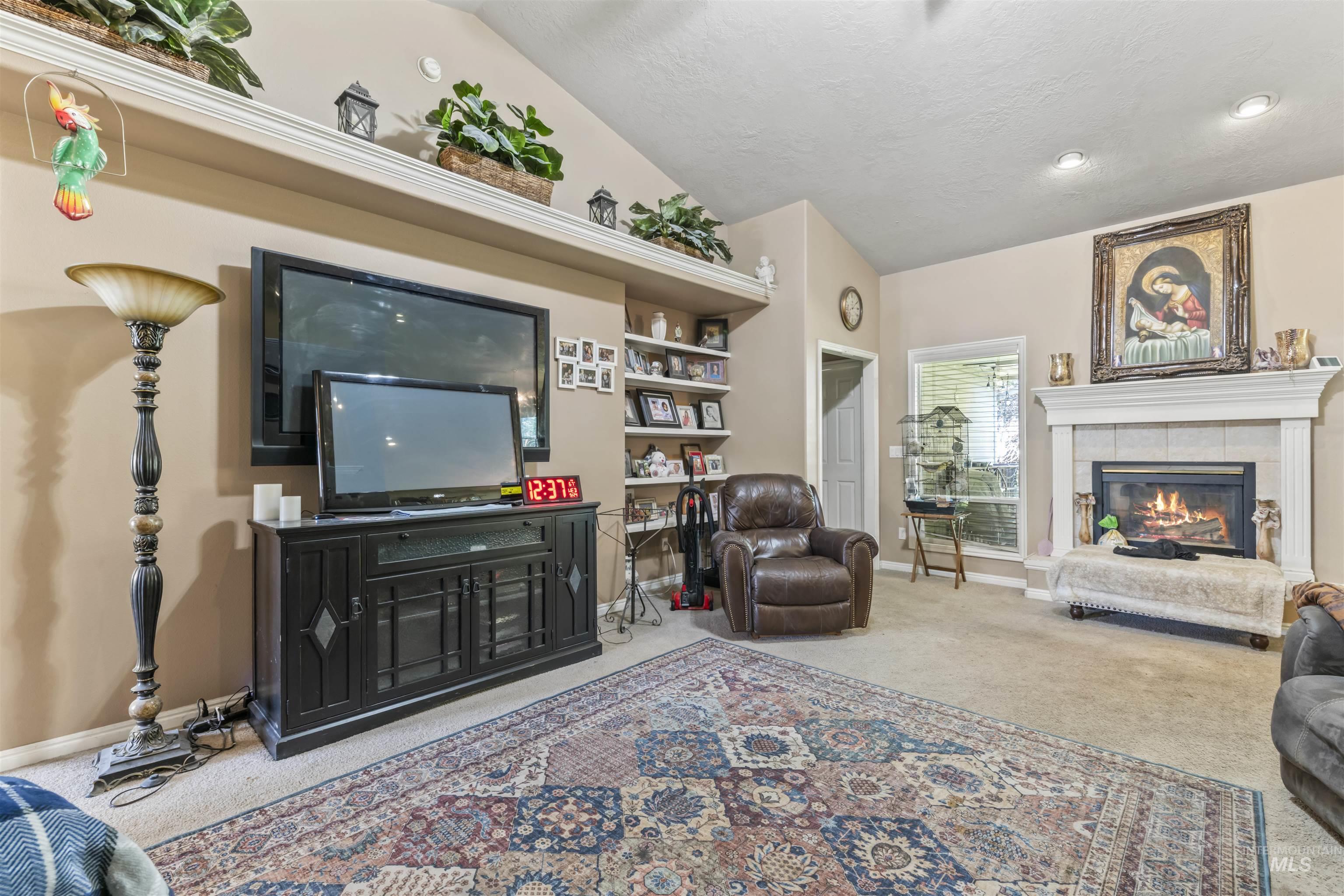 Living room featuring carpet flooring, vaulted ceiling, a textured ceiling, and a fireplace