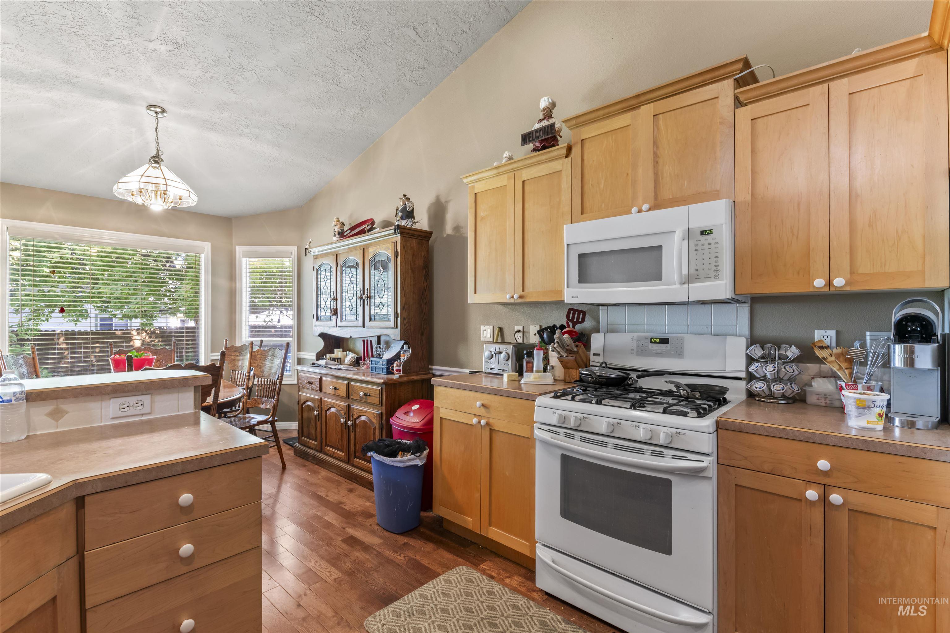 Kitchen with decorative backsplash, white appliances, a textured ceiling, dark wood-type flooring, and hanging light fixtures