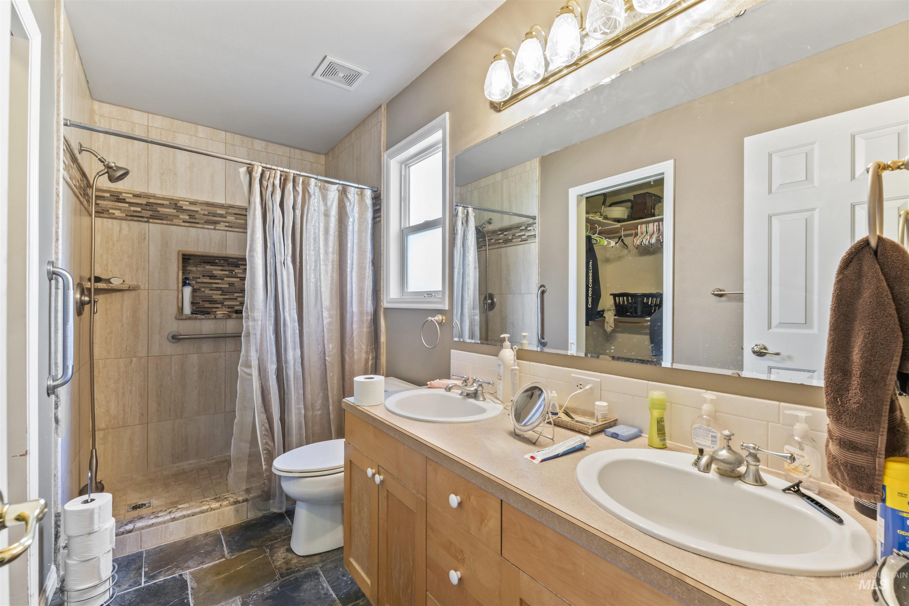 Full bathroom with a stall shower, double vanity, and stone tile floors