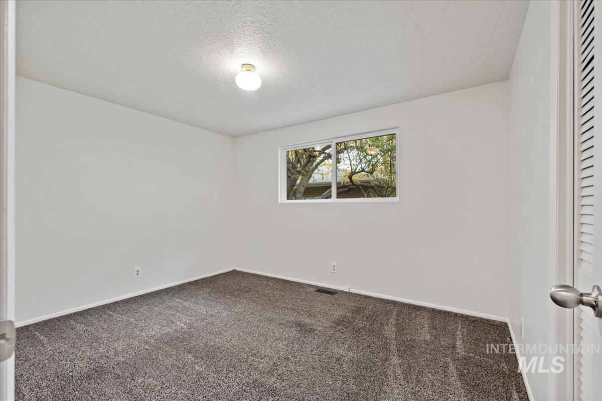 Empty room with a textured ceiling and dark colored carpet