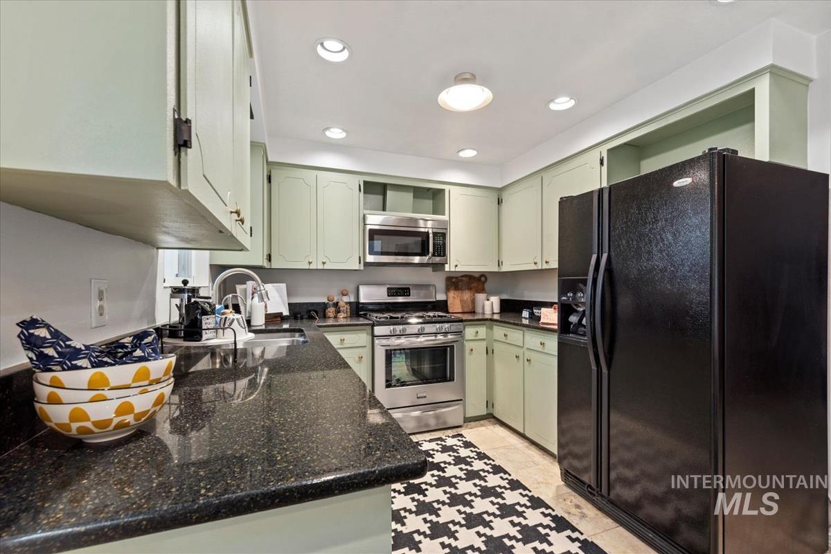 Kitchen with green cabinetry, appliances with stainless steel finishes, dark stone countertops, recessed lighting, and light tile patterned floors