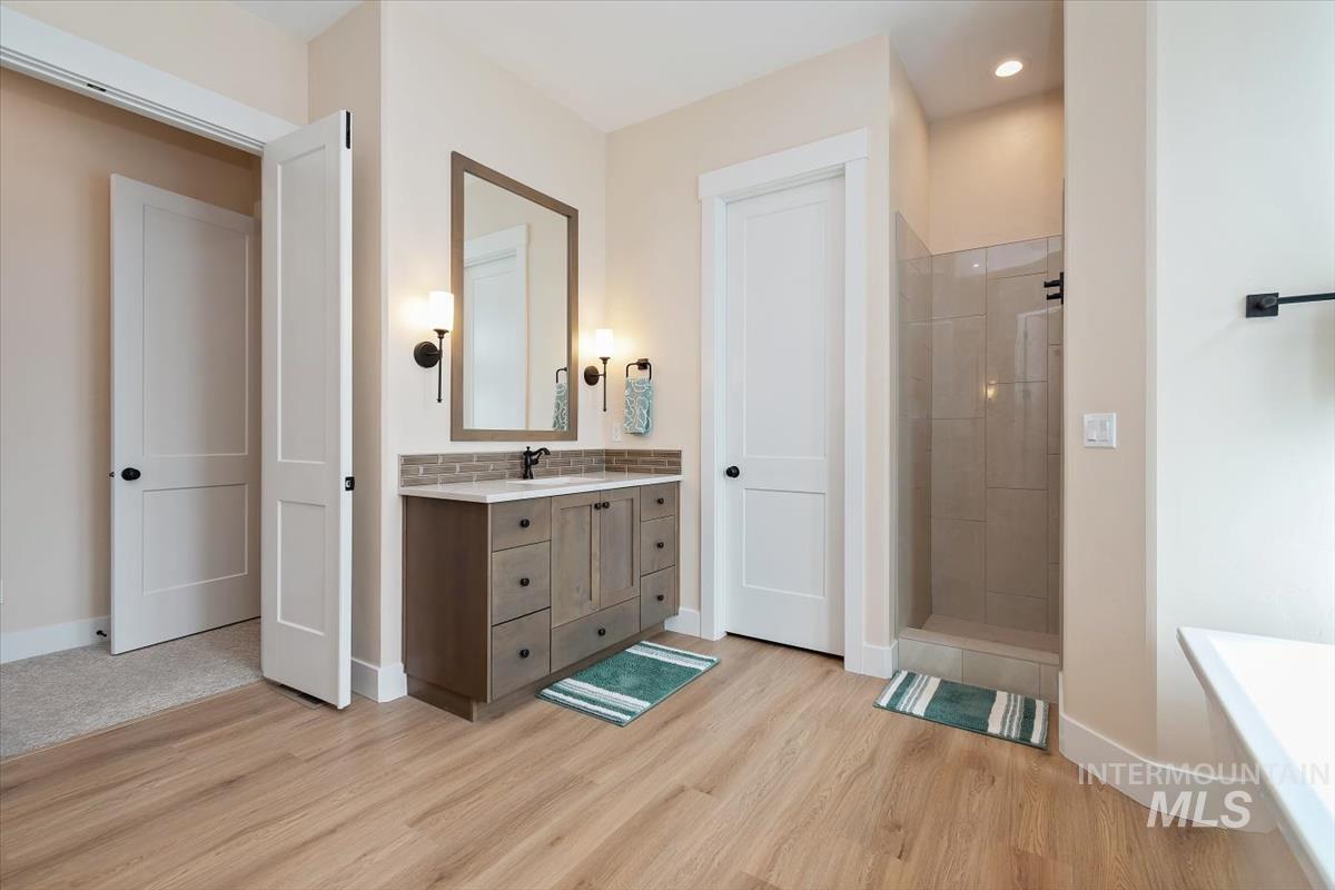 Bathroom featuring vanity, walk in shower, light wood-style floors, a freestanding bath, and recessed lighting