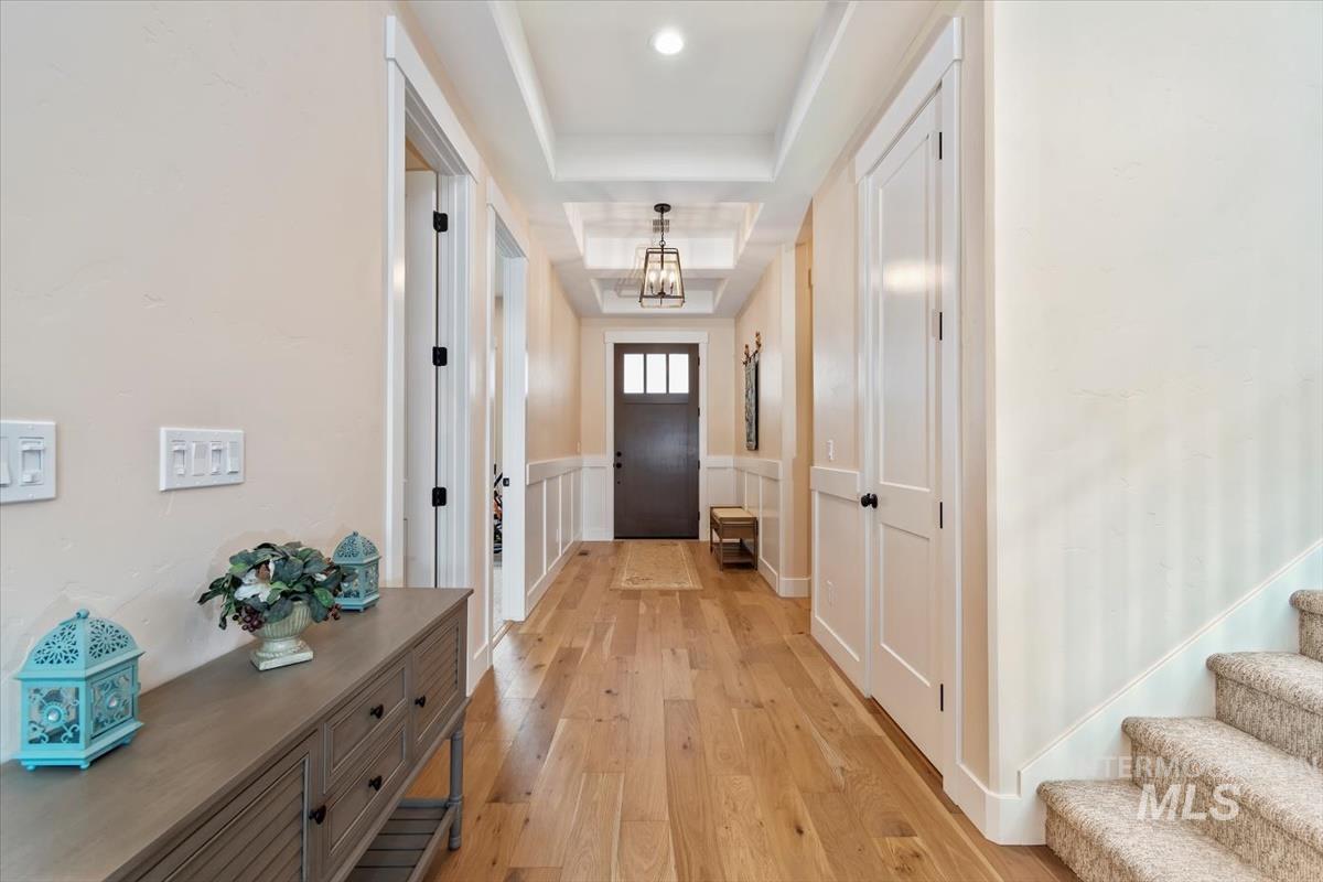 Doorway with a tray ceiling, wood finished floors, a chandelier, and a wainscoted wall