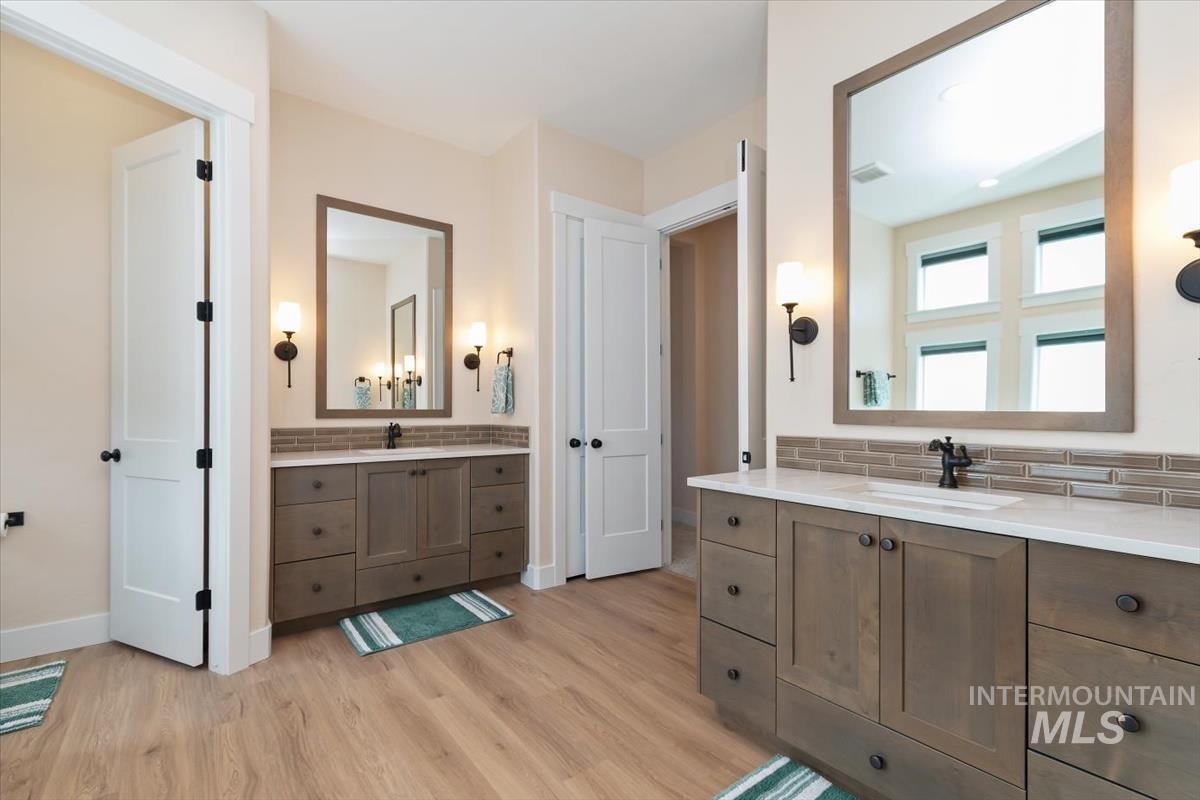 Bathroom with two vanities, tasteful backsplash, and light wood-style flooring
