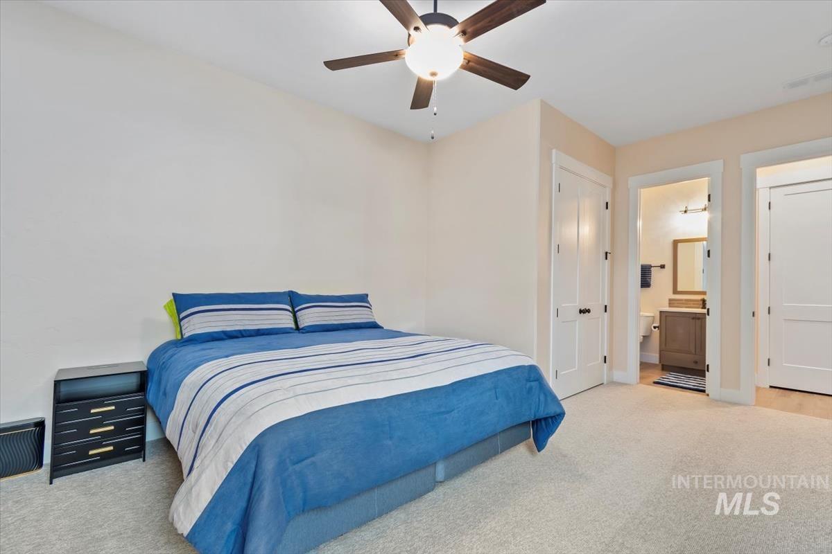 Bedroom with a closet, light colored carpet, ceiling fan, and ensuite bathroom