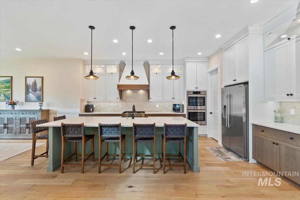 Kitchen featuring glass insert cabinets, a breakfast bar, appliances with stainless steel finishes, an island with sink, and recessed lighting