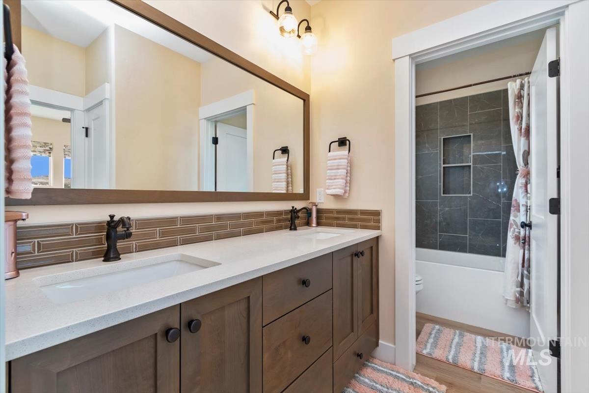 Bathroom featuring shower / bathtub combination with curtain, double vanity, tasteful backsplash, and light wood-style flooring