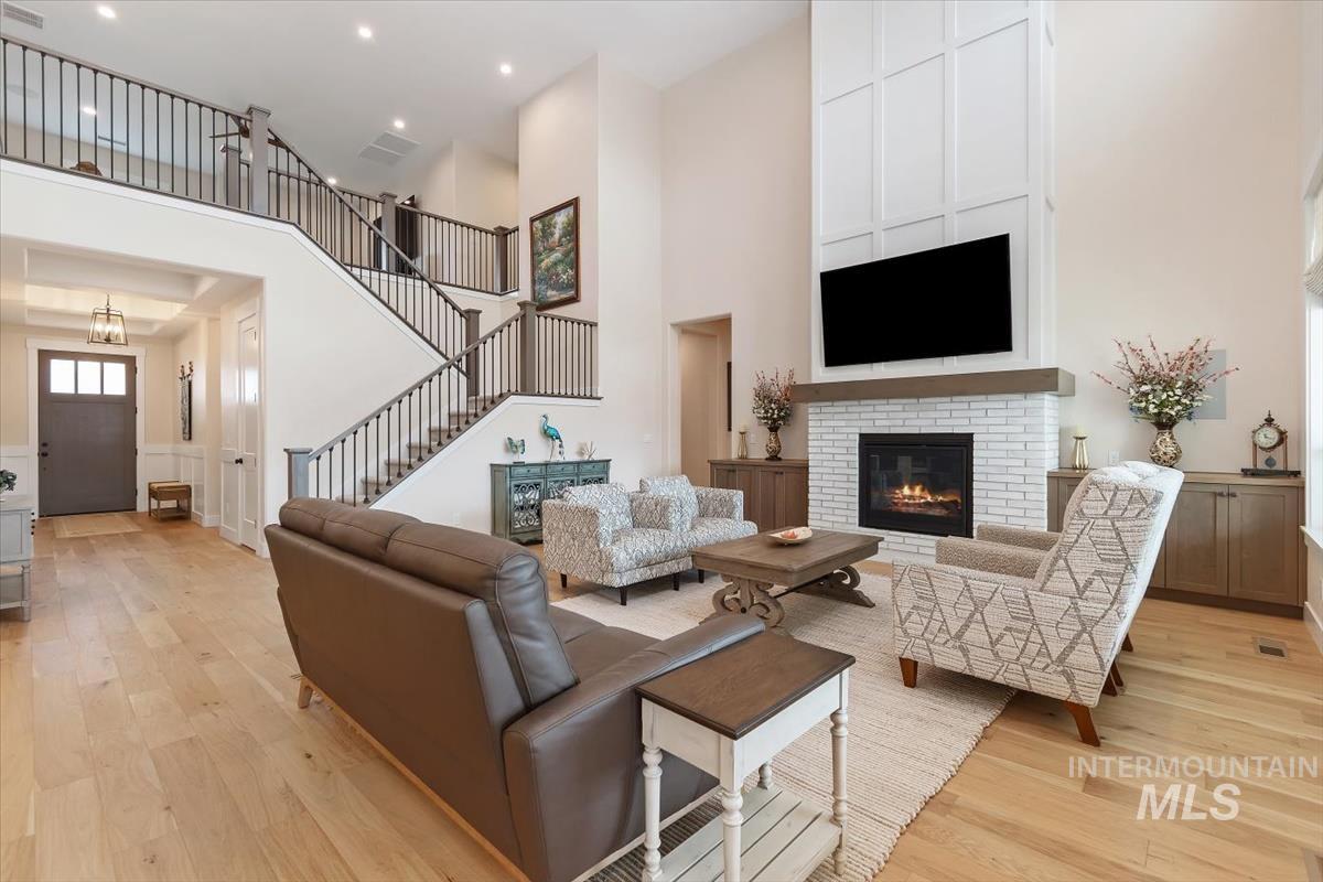 Living area featuring light wood-style flooring, a towering ceiling, a fireplace, stairway, and a decorative wall