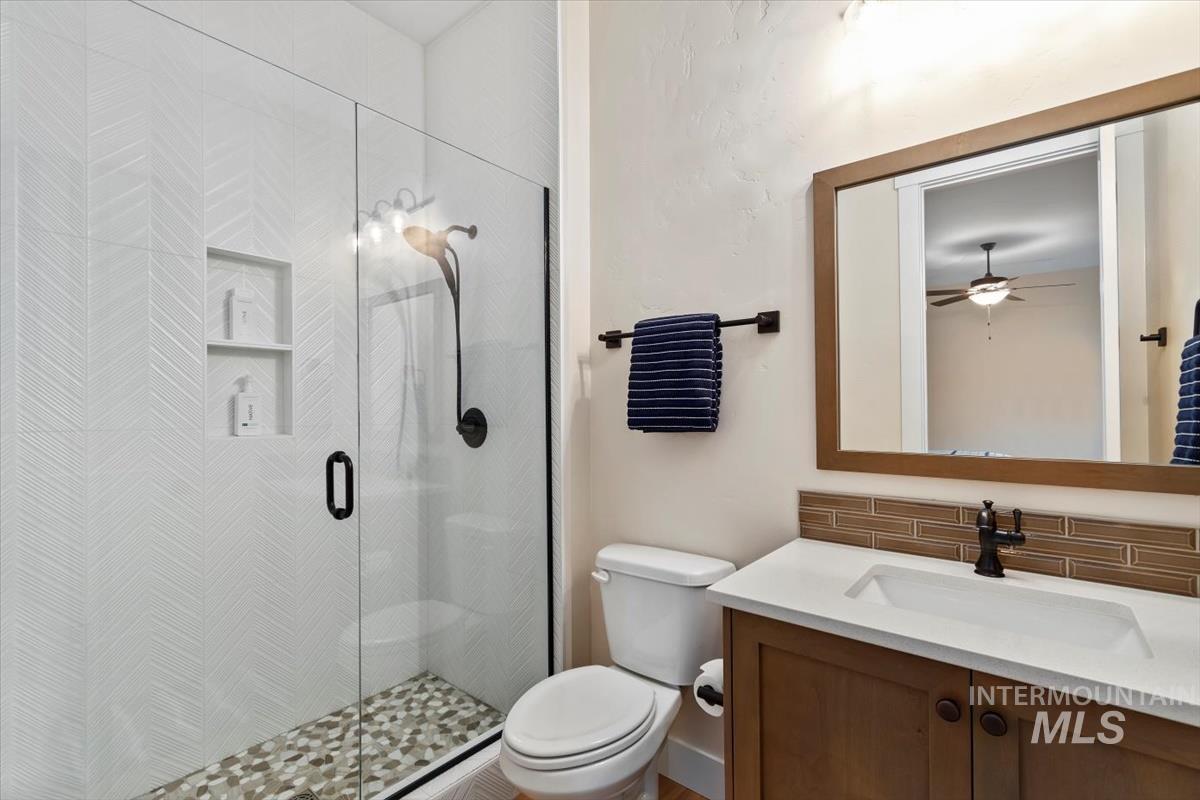 Full bath with vanity, a shower stall, tasteful backsplash, and ceiling fan