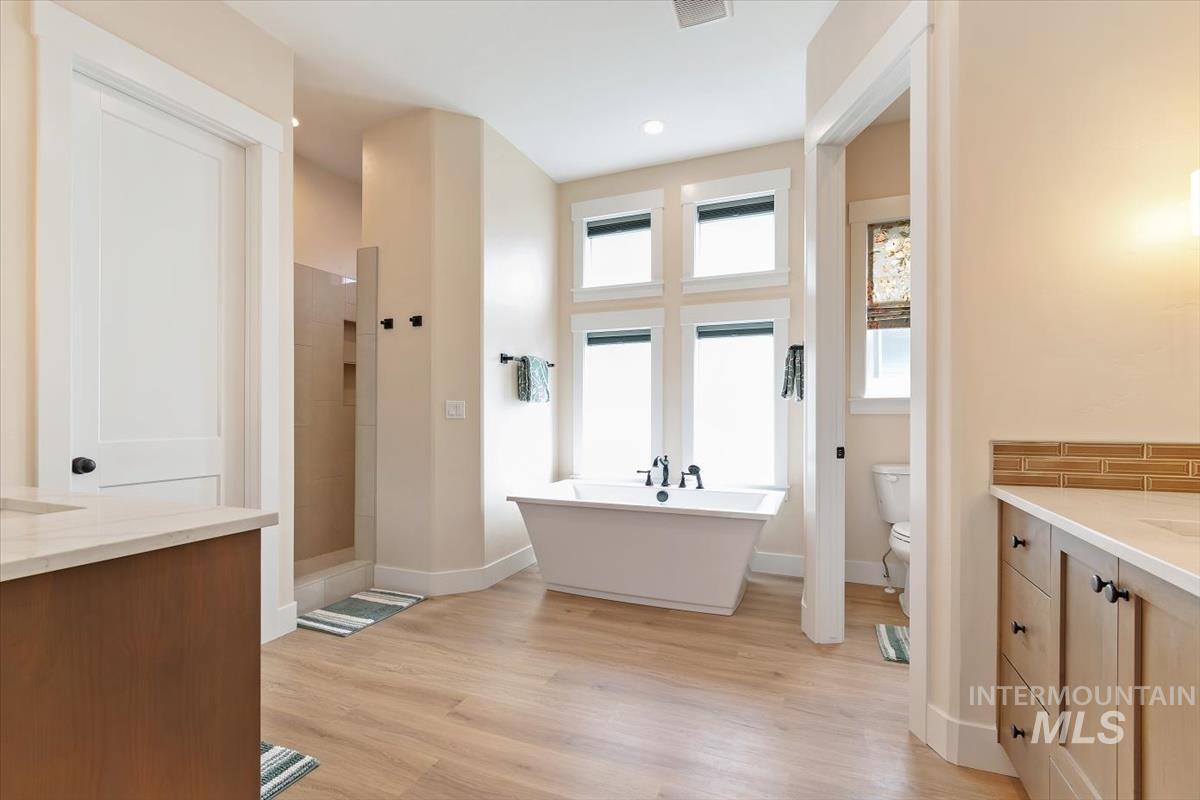 Bathroom featuring vanity, a tile shower, a freestanding tub, light wood-style flooring, and recessed lighting