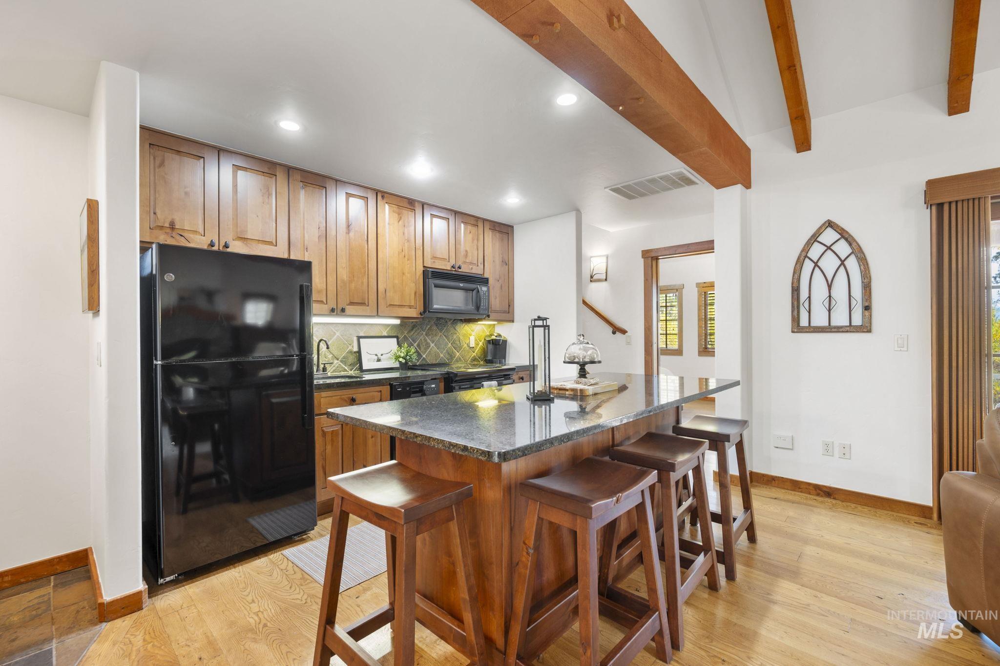 Kitchen with black appliances, backsplash, a kitchen bar, recessed lighting, and dark stone countertops