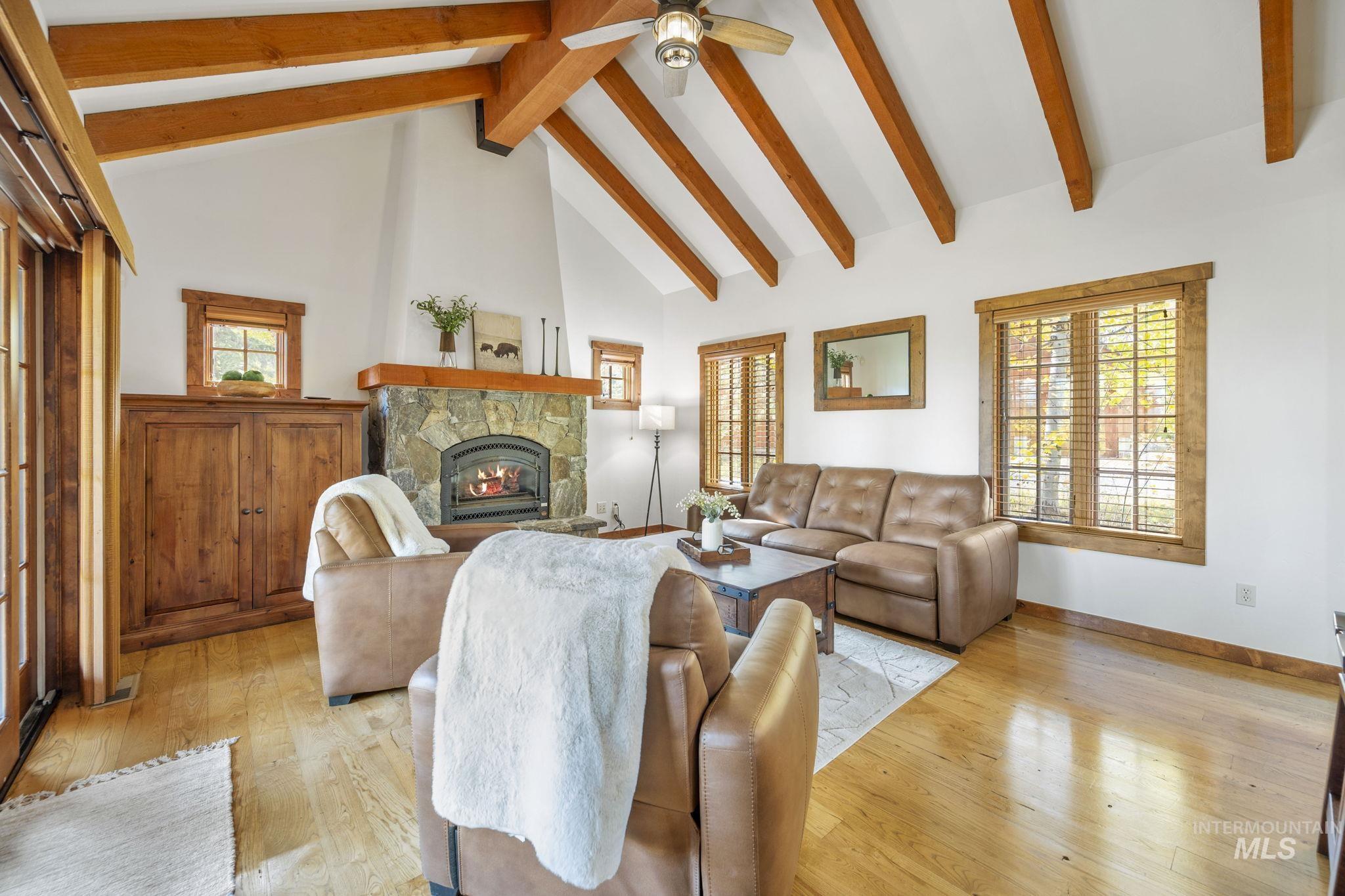 Living area with high vaulted ceiling, healthy amount of natural light, a fireplace, light wood-type flooring, and beamed ceiling