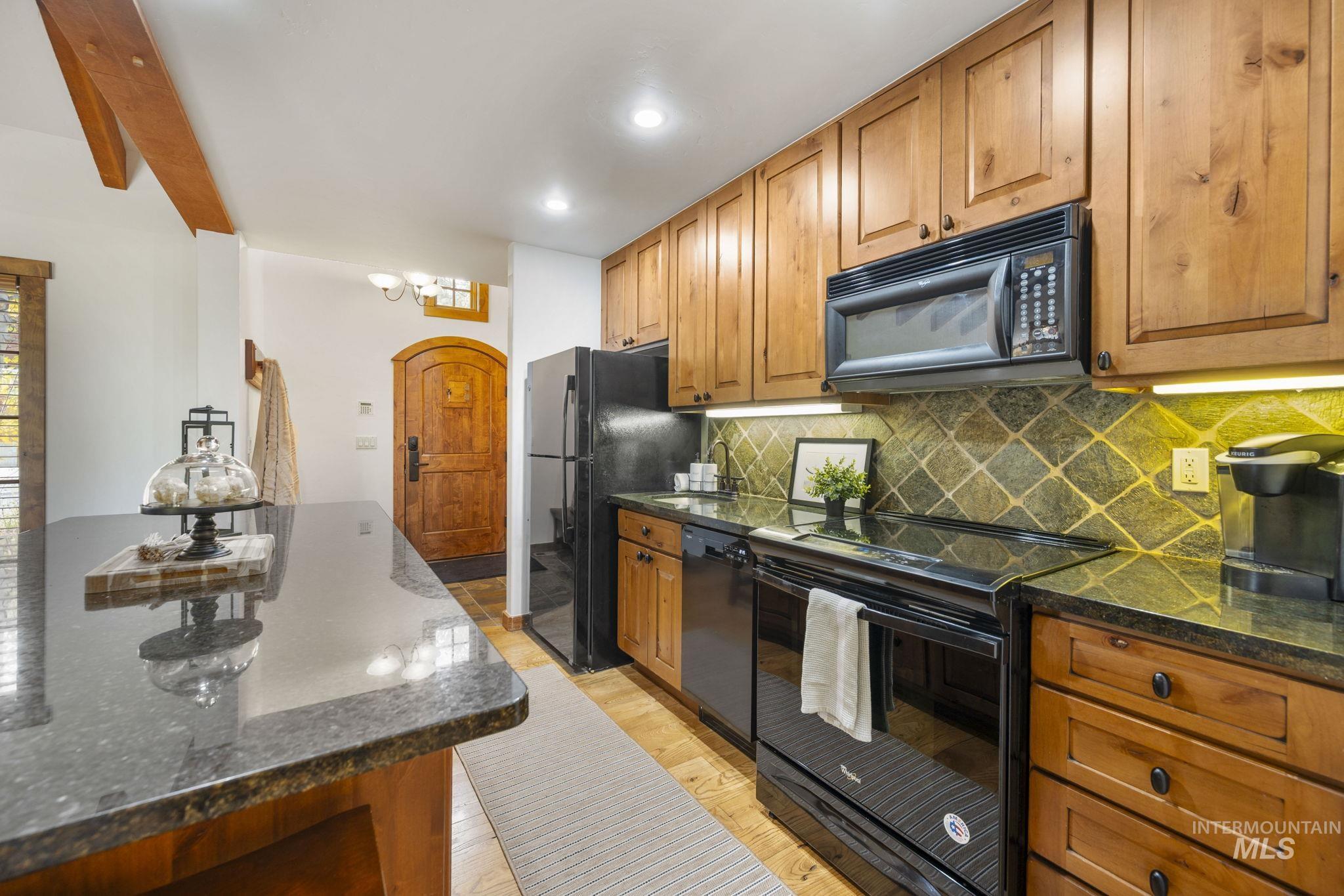 Kitchen with black appliances, tasteful backsplash, brown cabinetry, dark stone countertops, and recessed lighting