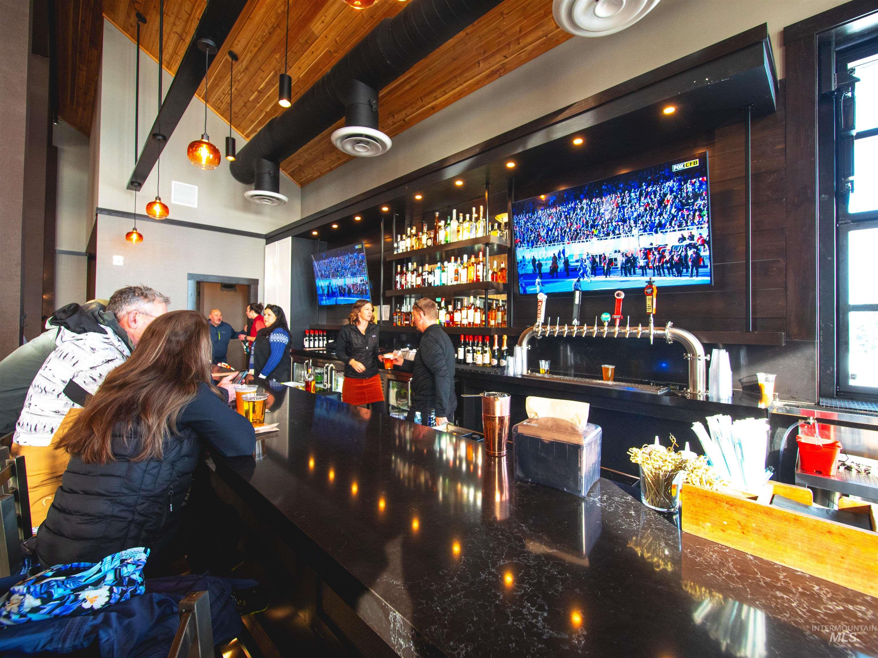 Community bar area featuring beam ceiling, dark brown cabinetry, decorative light fixtures, and dark stone counters