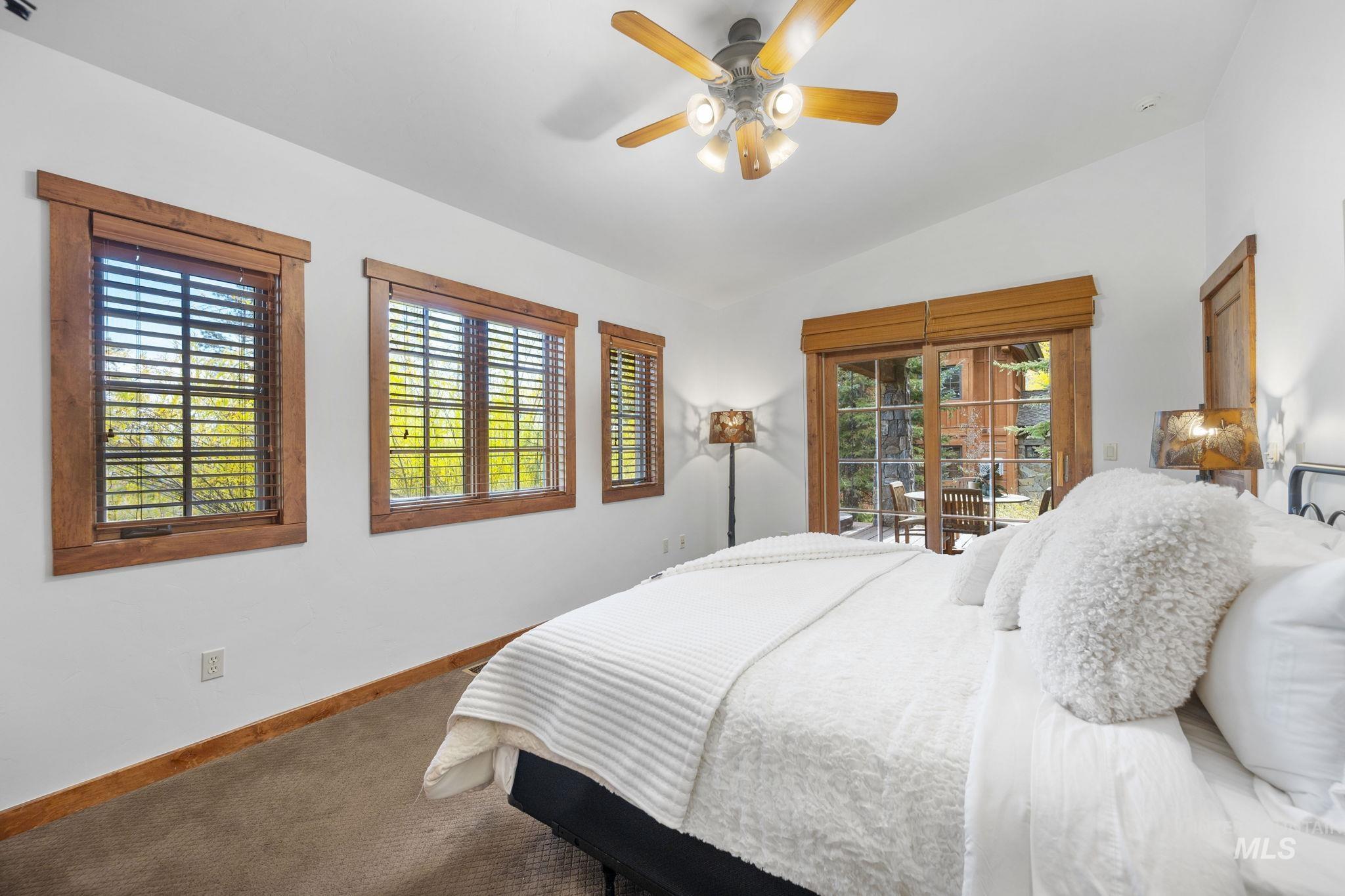 Bedroom with vaulted ceiling, multiple windows, access to exterior, carpet flooring, and a ceiling fan