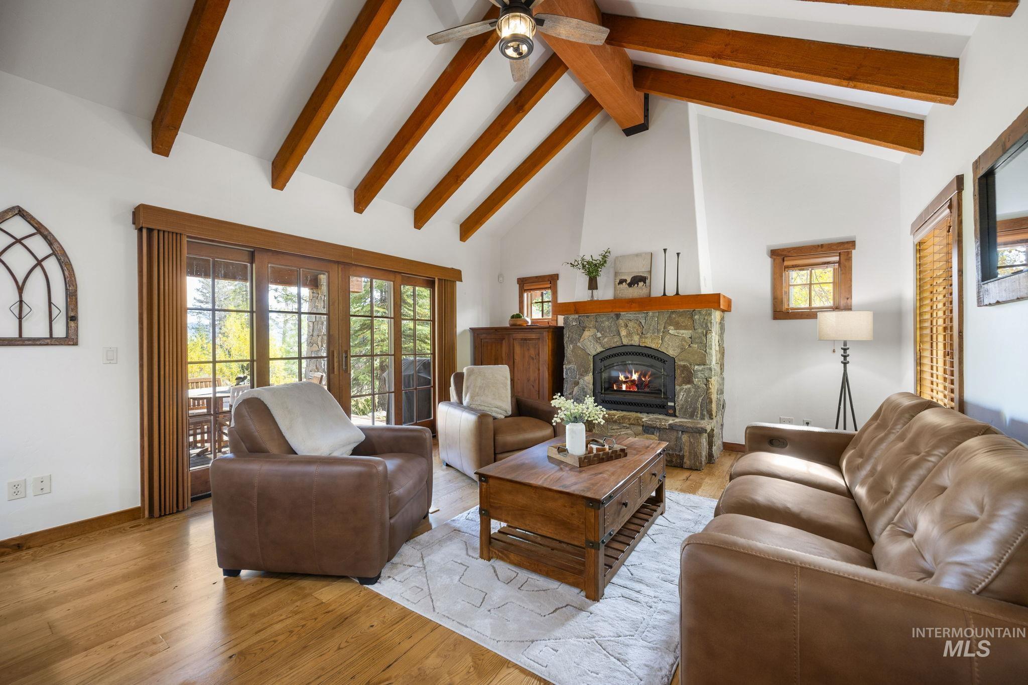 Living area with beamed ceiling, high vaulted ceiling, wood finished floors, plenty of natural light, and a stone fireplace