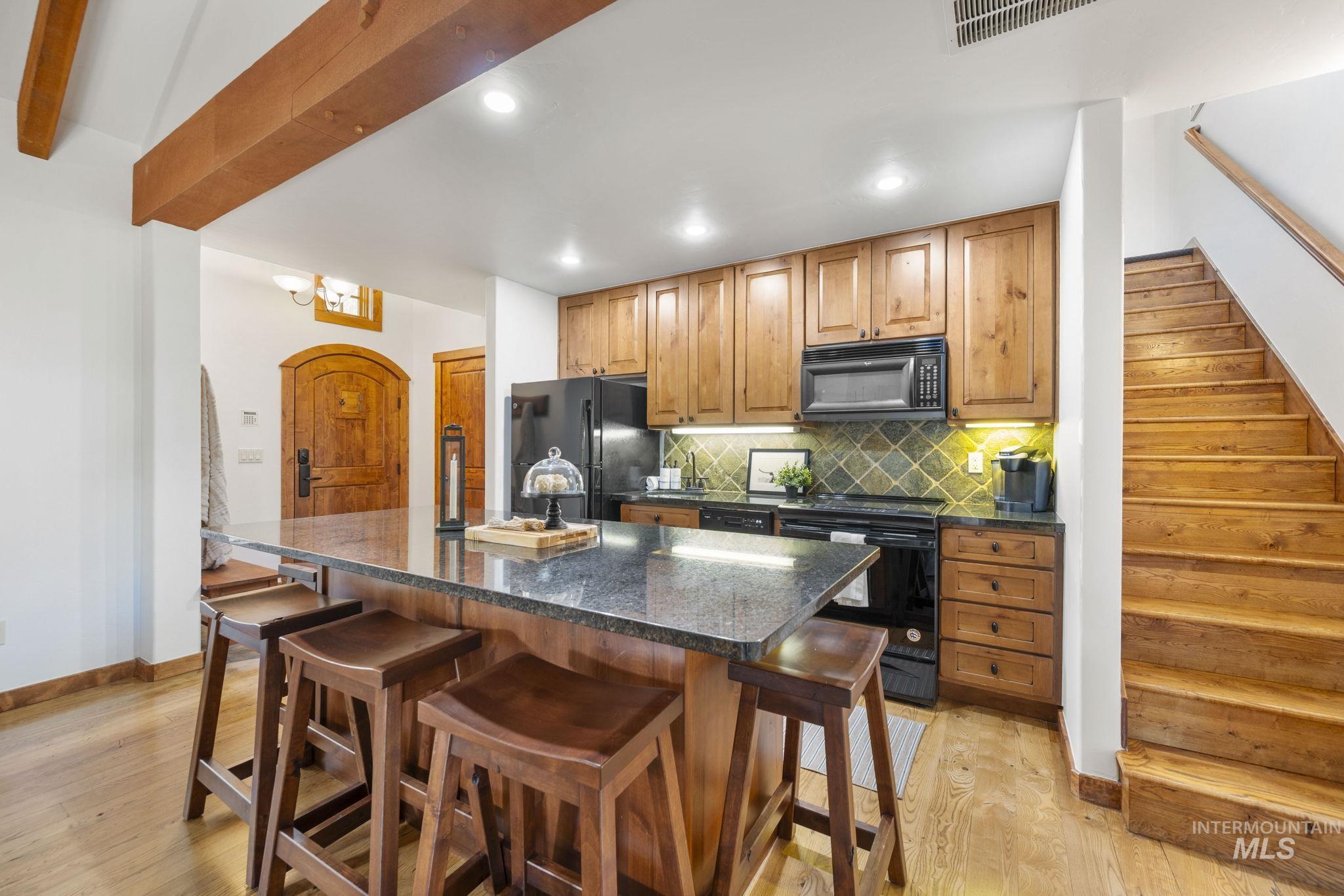 Kitchen with backsplash, black appliances, a breakfast bar area, light wood finished floors, and recessed lighting