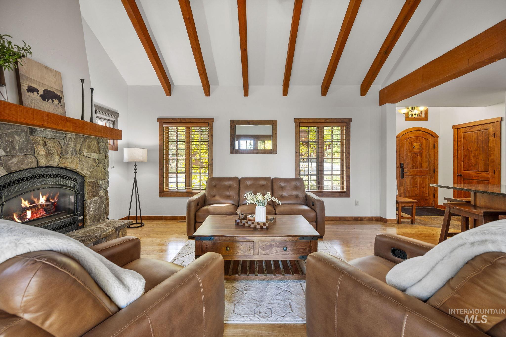 Living room with a stone fireplace, wood finished floors, beam ceiling, high vaulted ceiling, and a chandelier