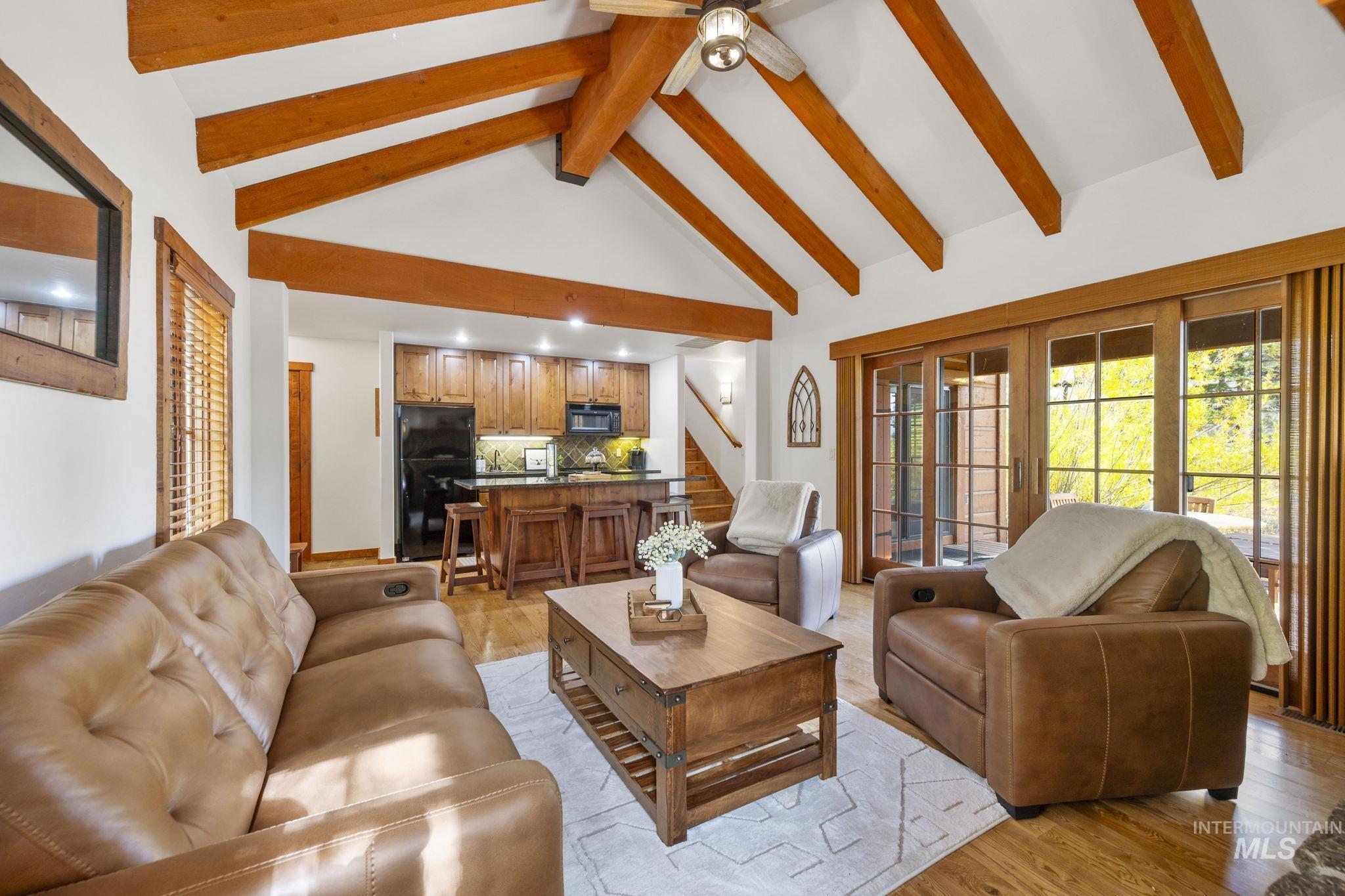 Living room with high vaulted ceiling, light wood-style floors, stairway, and beam ceiling