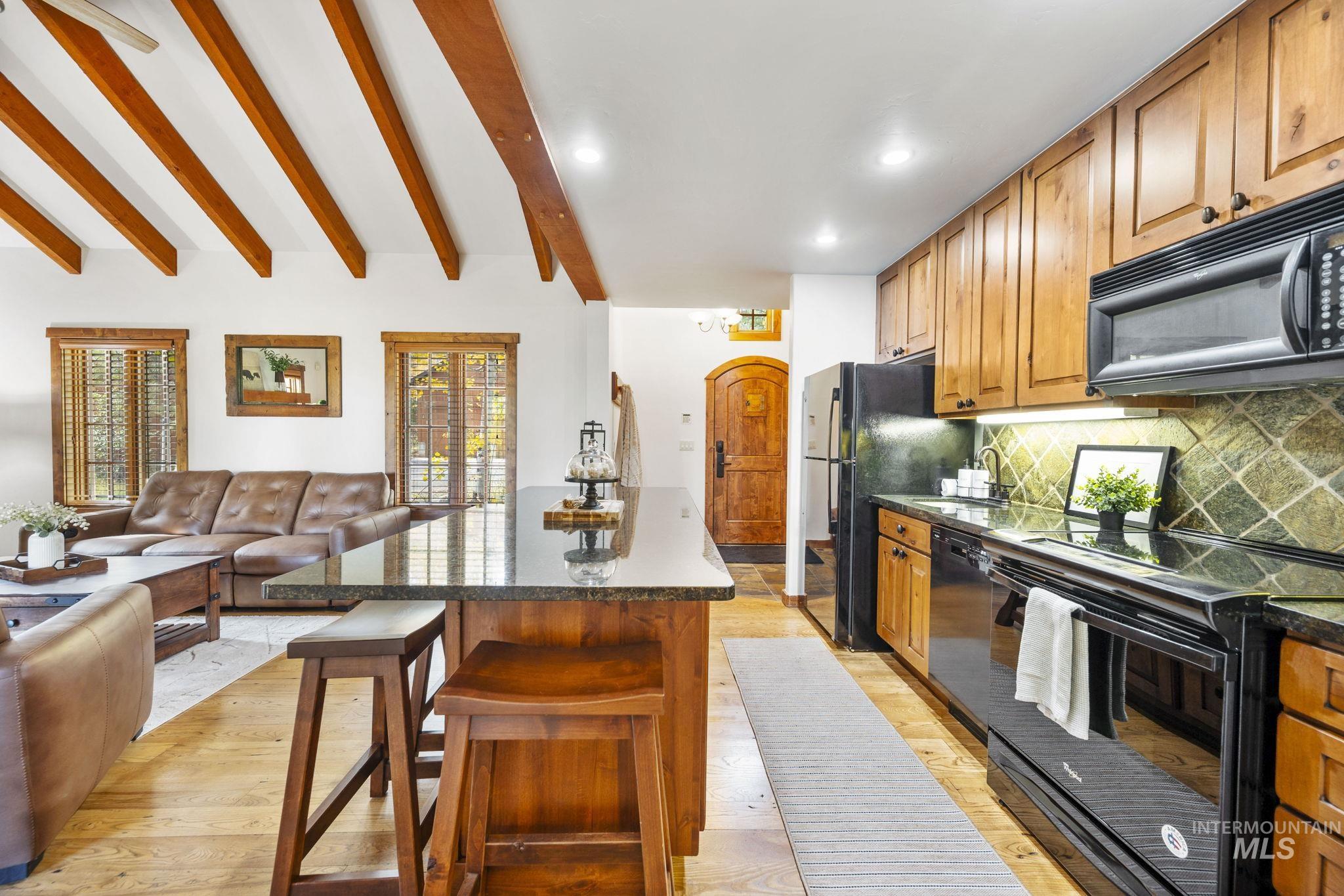 Kitchen with black appliances, a kitchen breakfast bar, open floor plan, backsplash, and beam ceiling