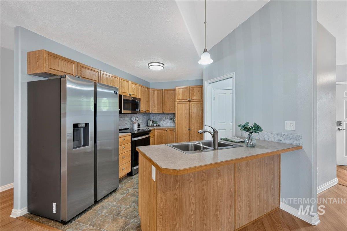 Kitchen featuring oak cabinetry, stainless steel appliances, a double basin sink, neutral countertops, and tile flooring