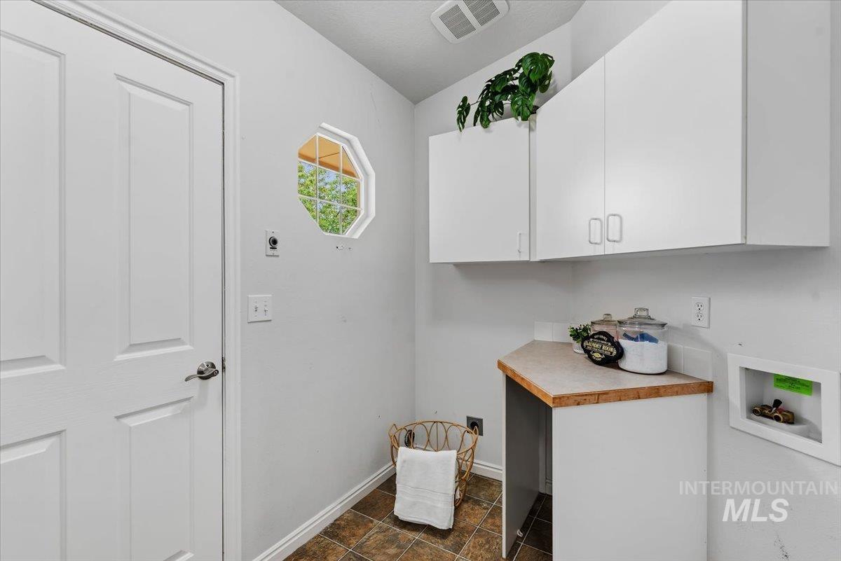 Utility room featuring a paneled door, octagonal accent window, white upper cabinetry, a built-in counter with wood-finish trim, and tiled flooring