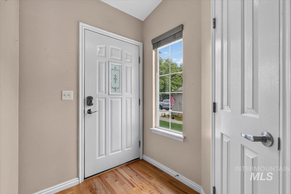 Entryway featuring wood-finish flooring, a white paneled door with decorative glass inlay, and a window with a window blind